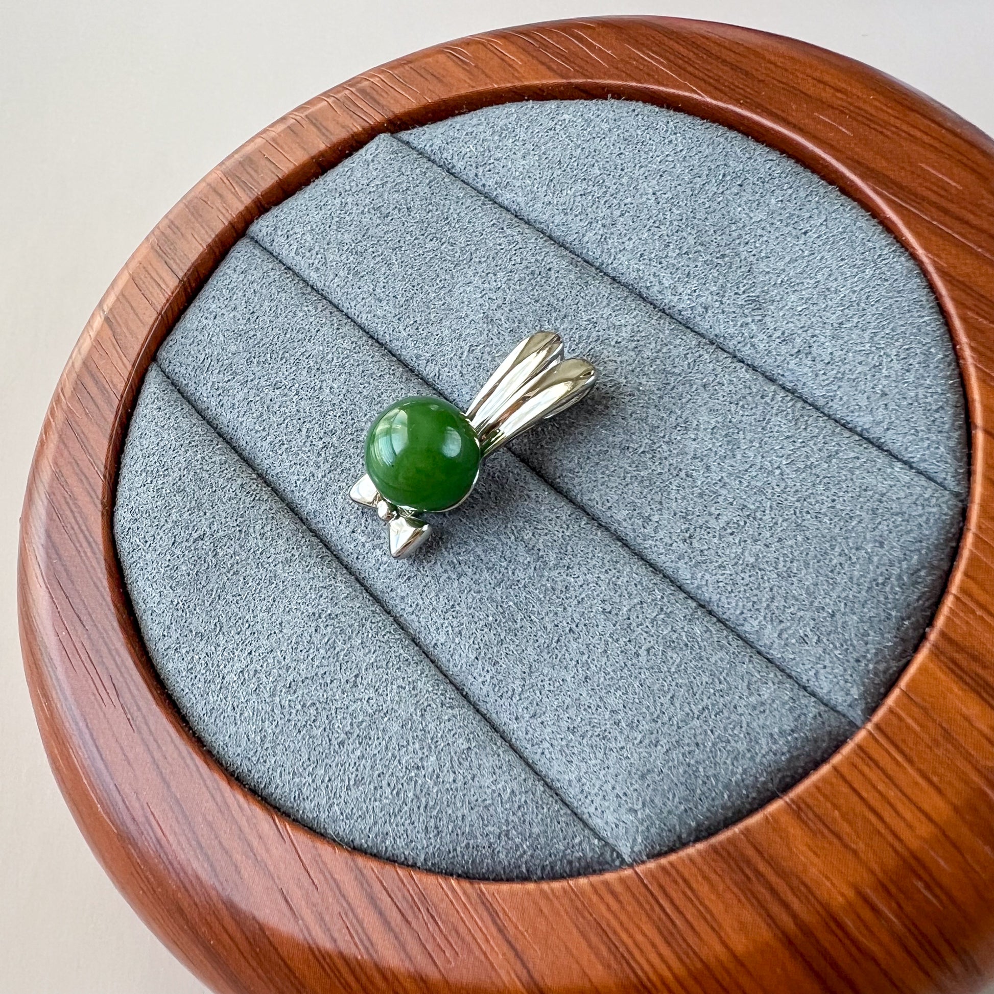 Top-down view of green nephrite jade rabbit pendant with sterling silver bowtie on gray velvet display tray