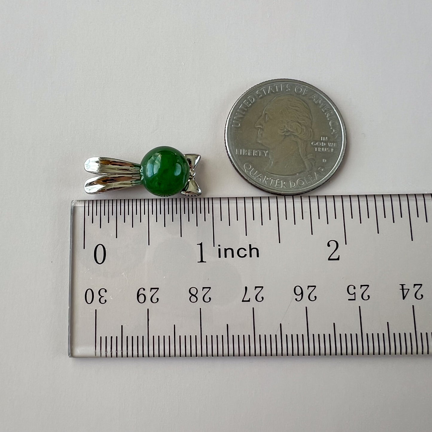 Green nephrite jade rabbit pendant with sterling silver bowtie, glossy finish, shown beside a quarter and ruler for scale