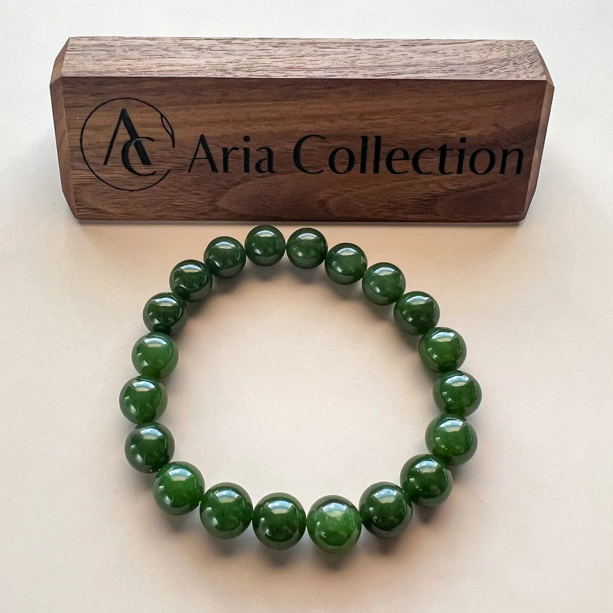 Green beaded bracelet displayed flat beside a branded wooden box on a neutral background