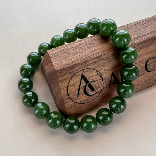 Glossy dark green bead bracelet draped over a wooden display box, angled side view