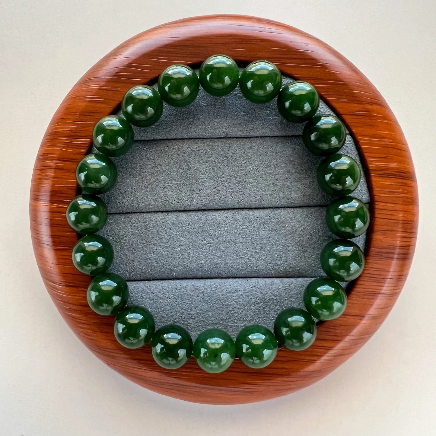 Round green beaded bracelet arranged on a wooden oval display tray with gray velvet insert