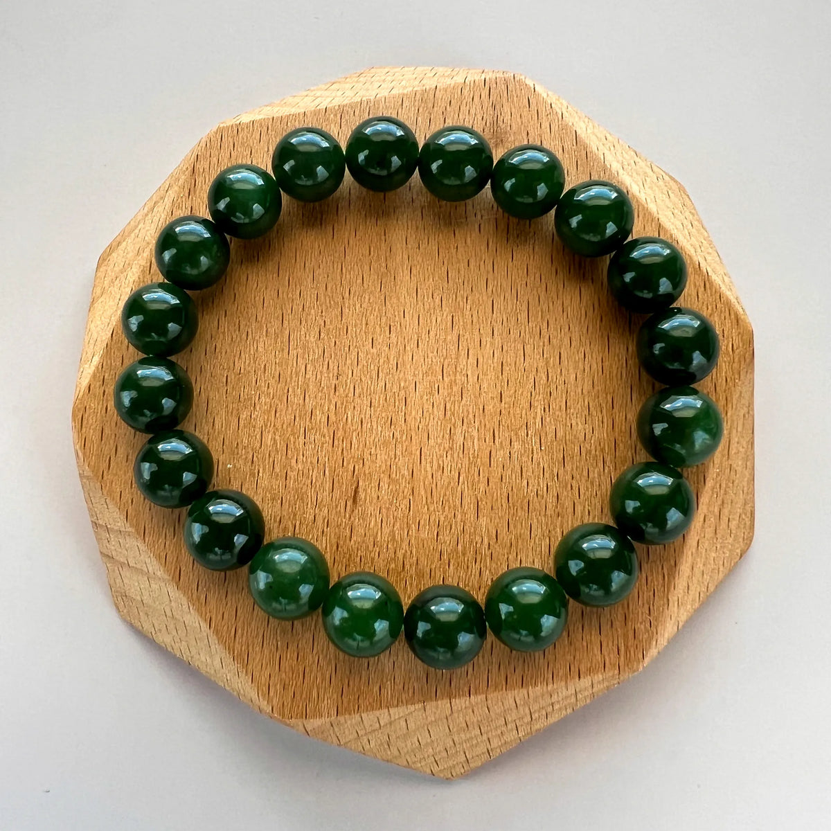Glossy green bead bracelet centered on a faceted wooden stand, top view on neutral background