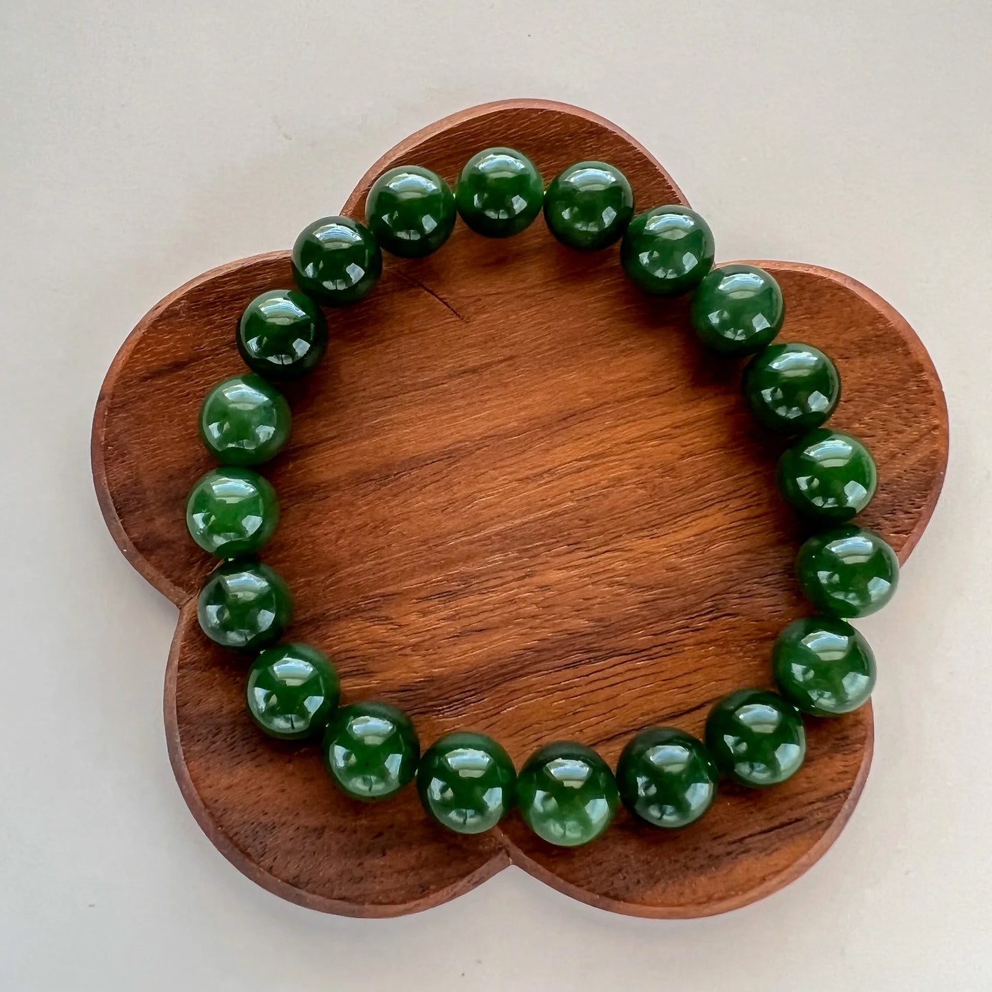 Dark green beaded bracelet shown on a flower-shaped wooden display, polished round beads visible