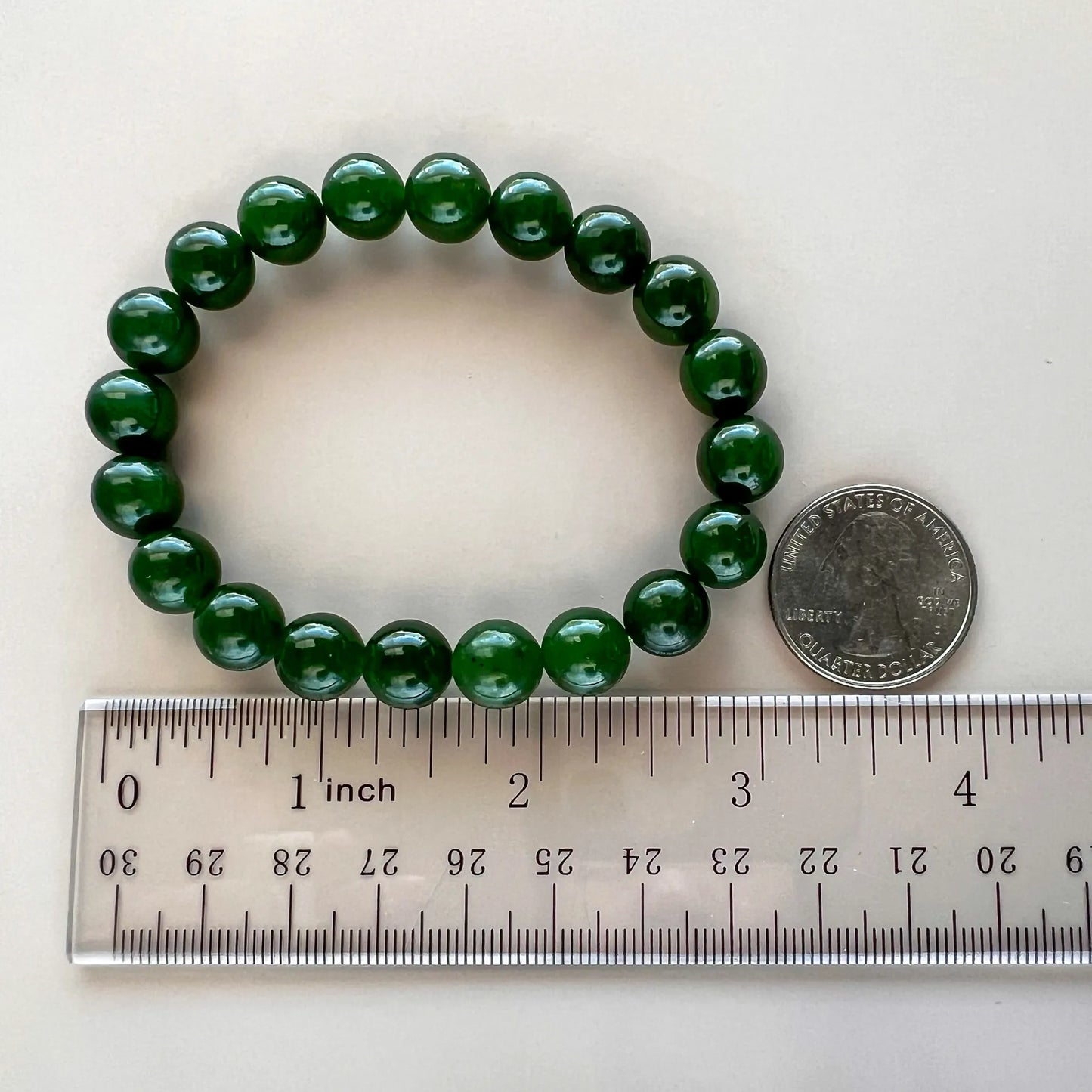 Deep green round-bead bracelet shown beside a ruler and quarter for scale