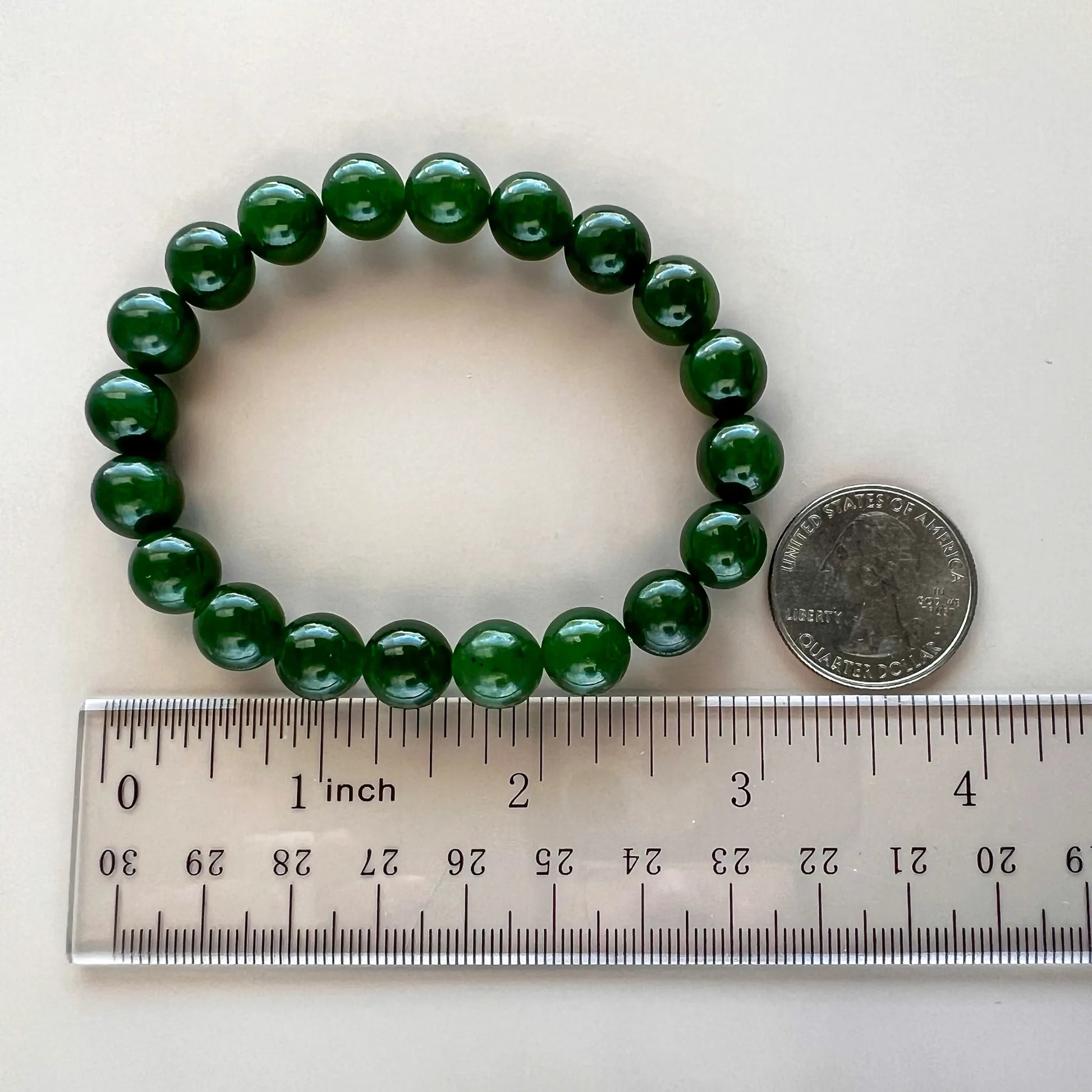 Deep green round-bead bracelet shown beside a ruler and quarter for scale