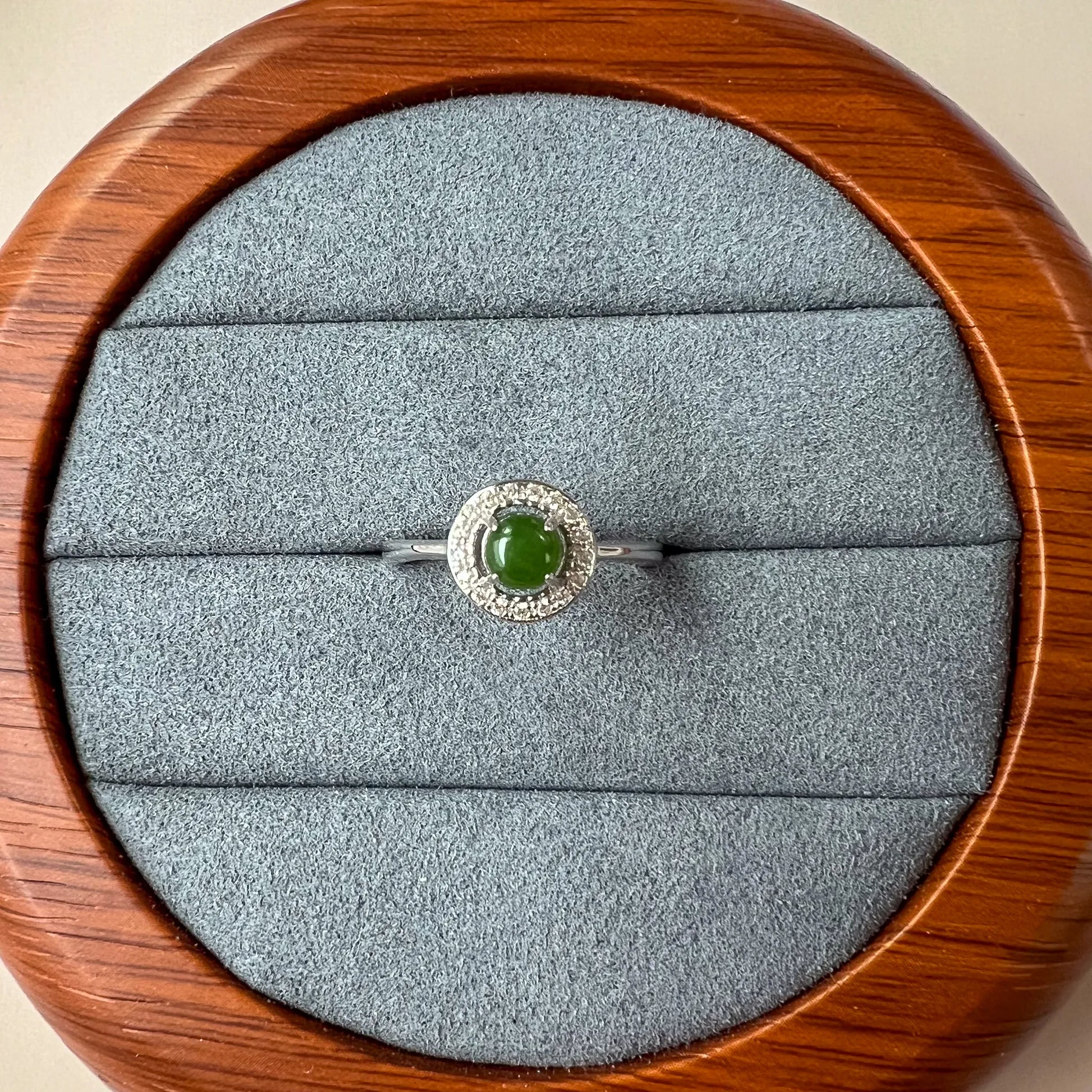 Top view of silver ring with green cabochon and pavé halo on gray velvet display