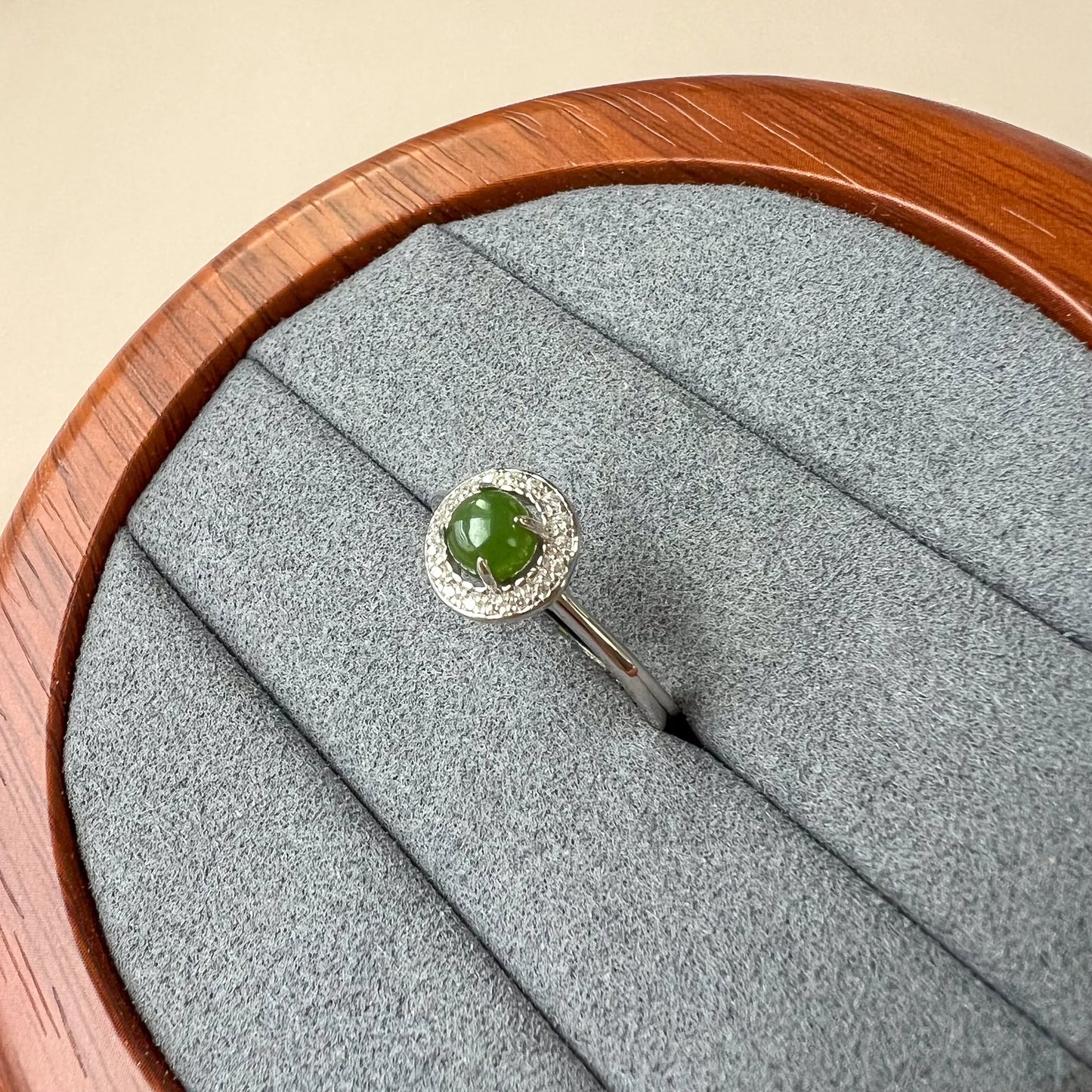 Angled view of sterling silver ring with green stone and halo of clear accents