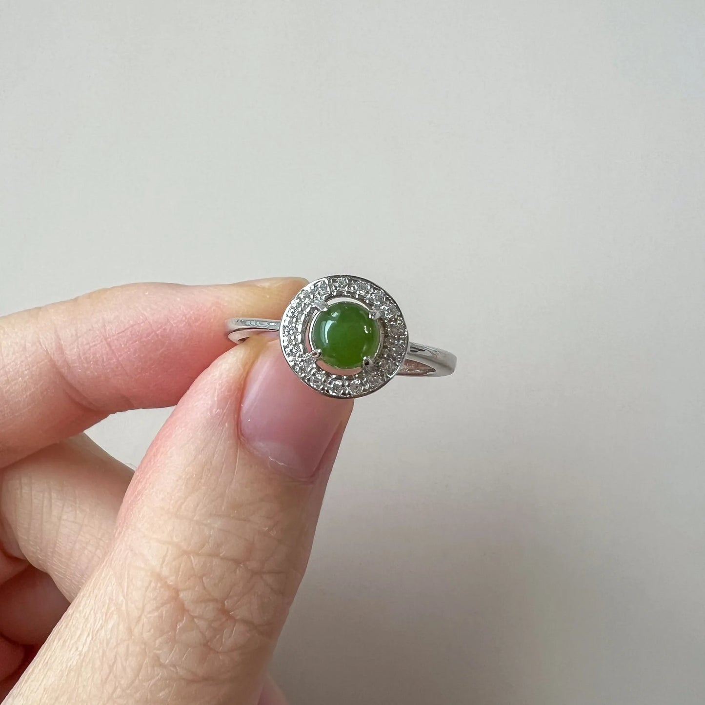 Close view of green cabochon stone in prong setting with halo accents and slim silver-tone band
