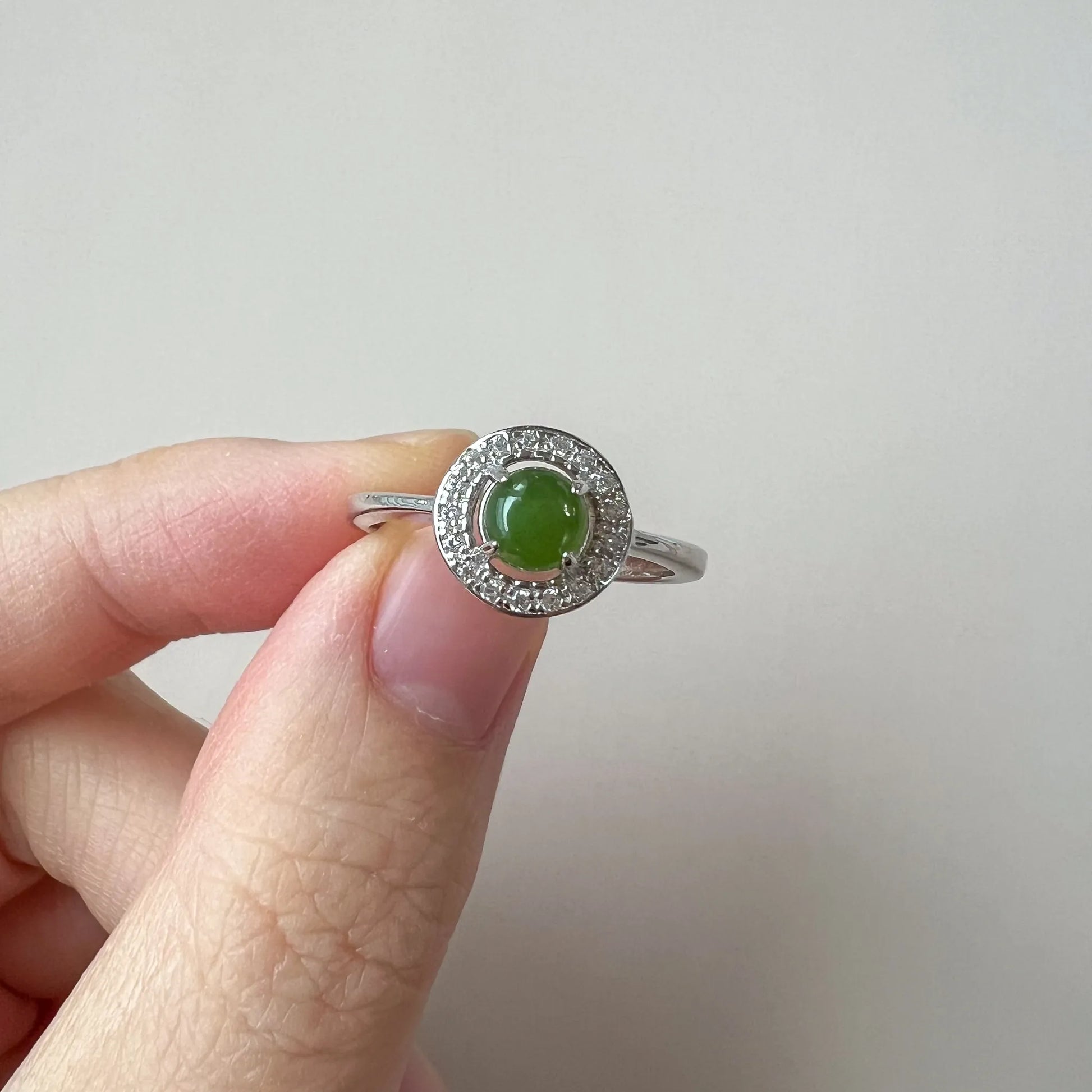 Close view of green cabochon stone in prong setting with halo accents and slim silver-tone band