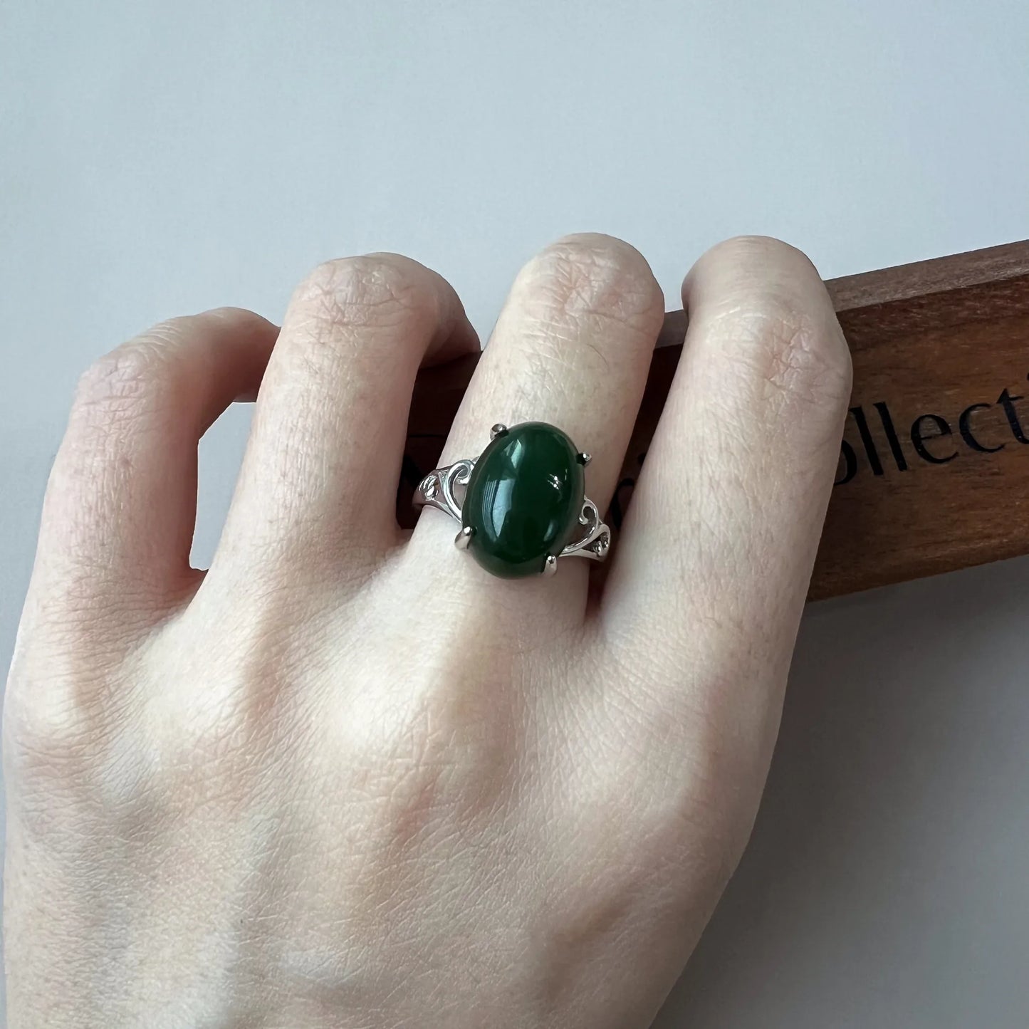 On-hand view of oval green gemstone ring with ornate silver band