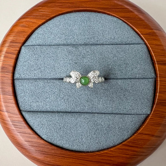 Top view of silver ring with green cabochon center and butterfly motif on gray velvet tray