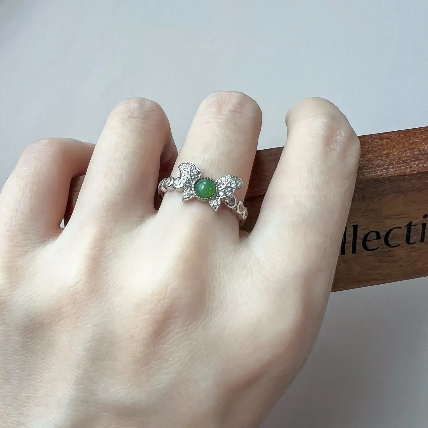 Ring worn on hand showing butterfly-inspired silver setting with green gemstone and pavé accents