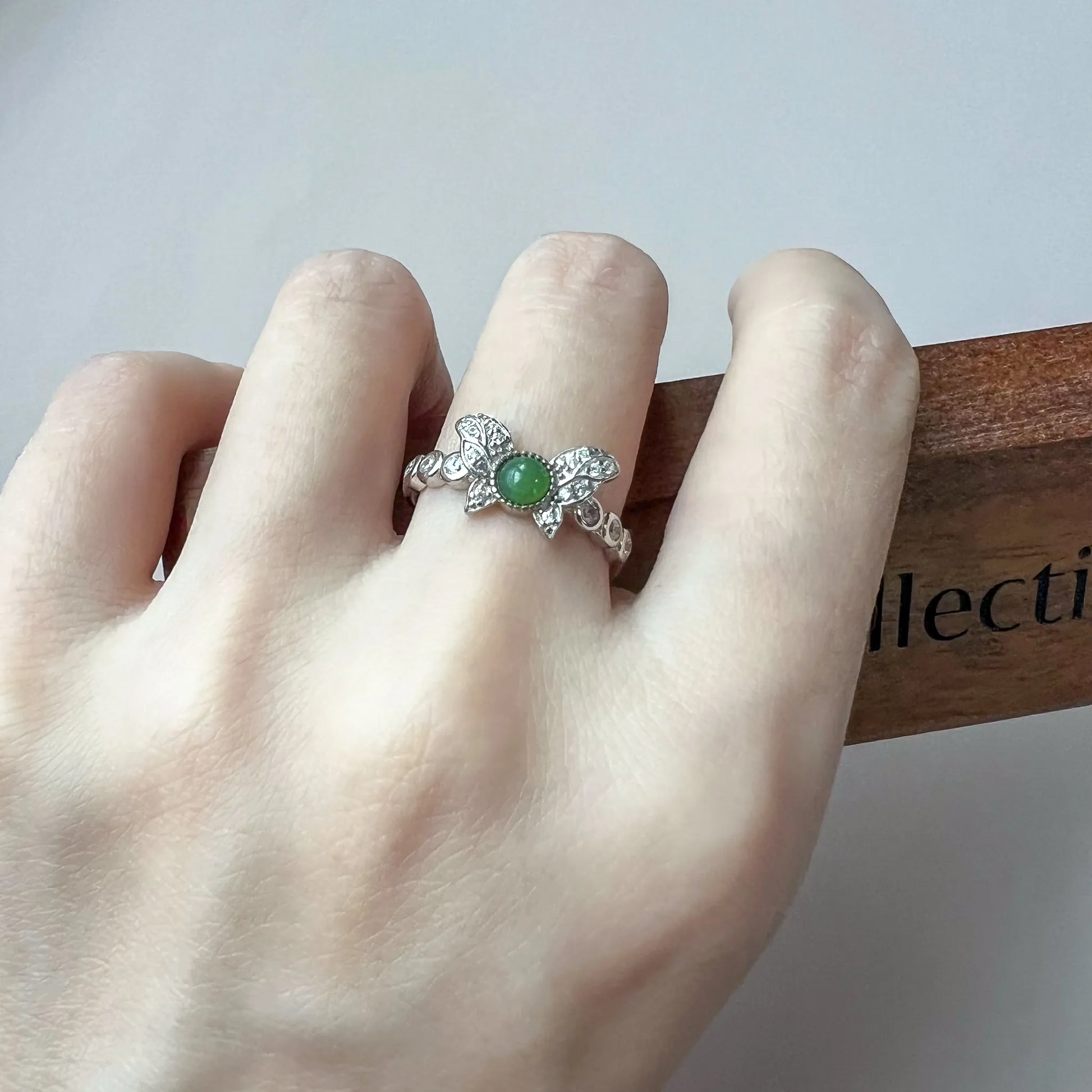 Ring worn on hand showing butterfly-inspired silver setting with green gemstone and pavé accents