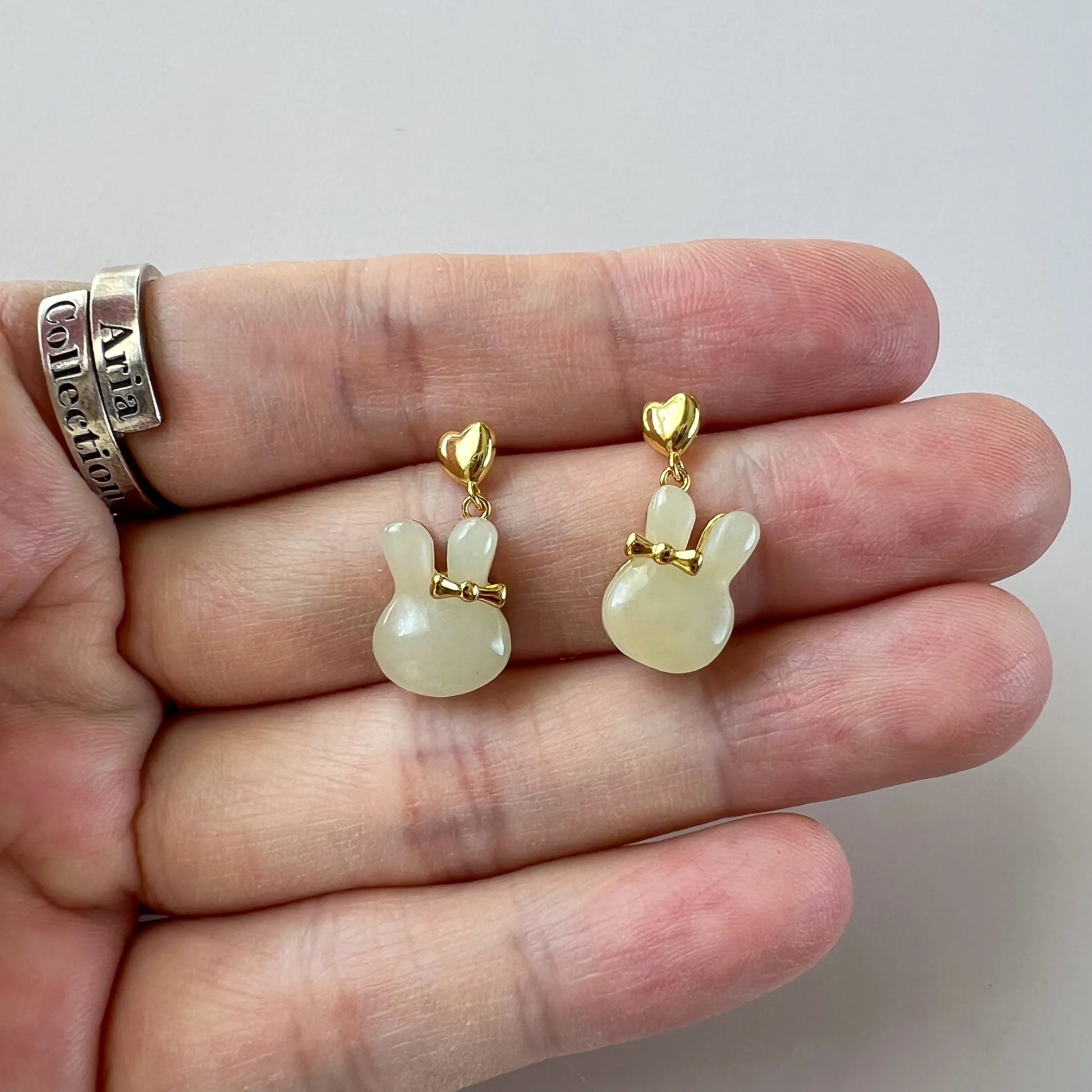 Close-up of bunny rabbit nephrite jade stud earrings with gold-plated silver bows held in hand, polished finish