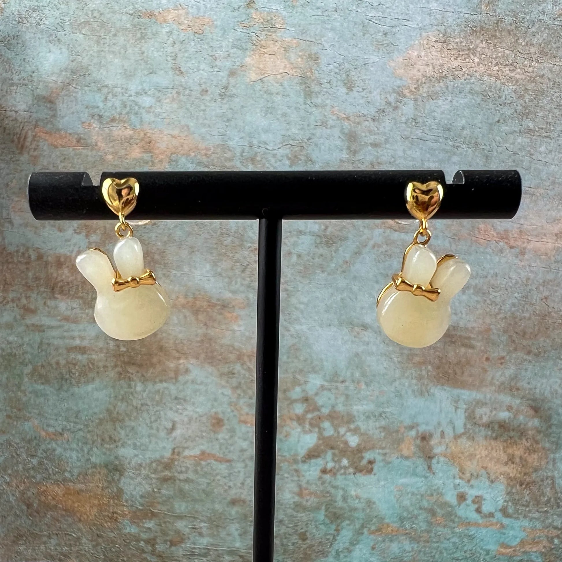 Bunny rabbit nephrite jade stud earrings with gold-plated silver bows on black display stand, front view