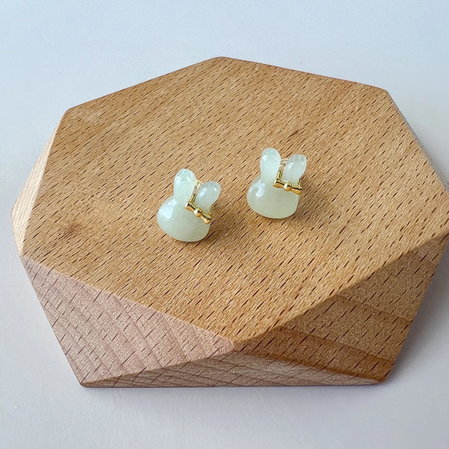Front view of pale green jade bunny stud earrings on a wooden display