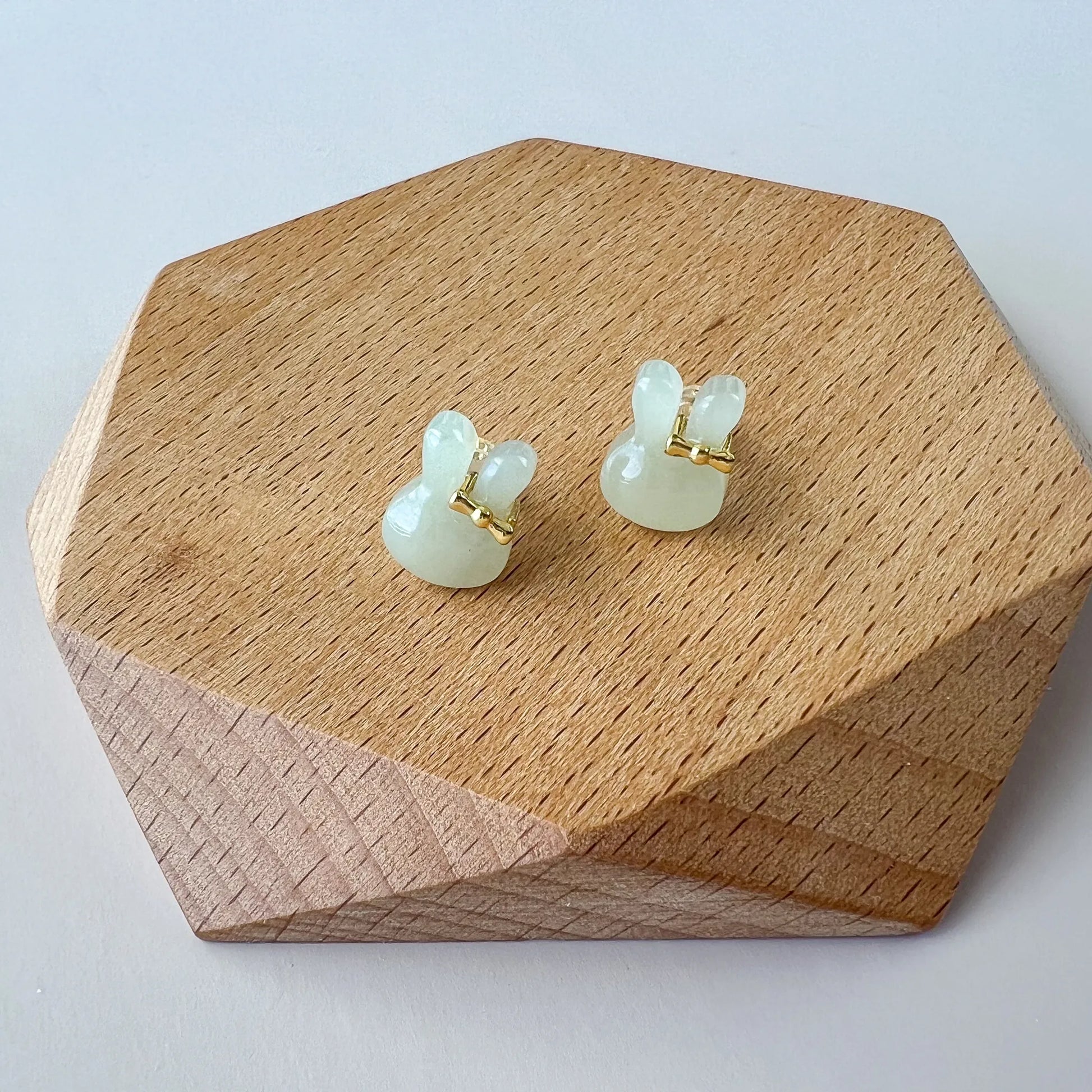 Front view of pale green jade bunny stud earrings on a wooden display