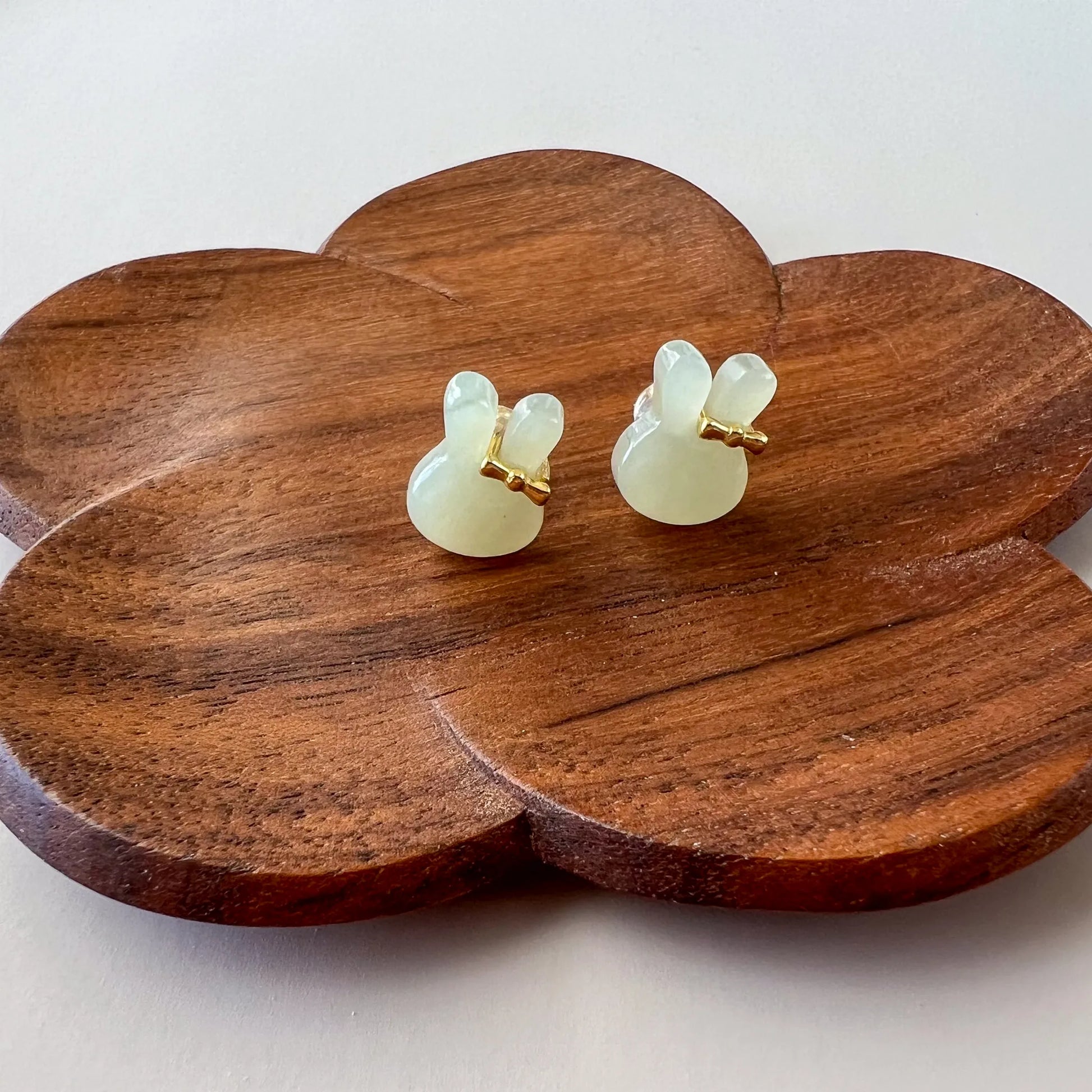 Front view of jade bunny stud earrings on a flower-shaped wooden tray
