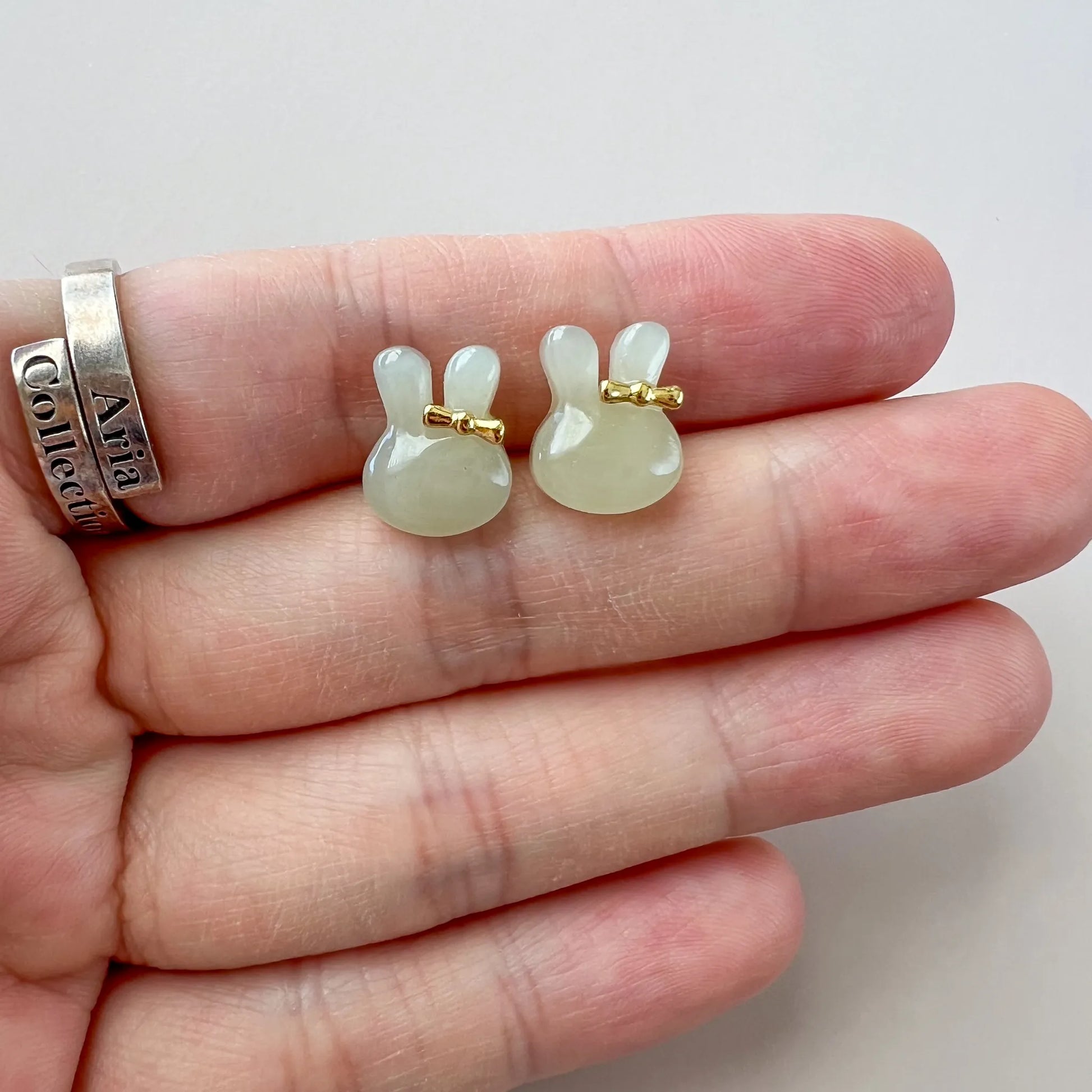 Close-up of jade bunny stud earrings shown on a hand, with gold-tone accents