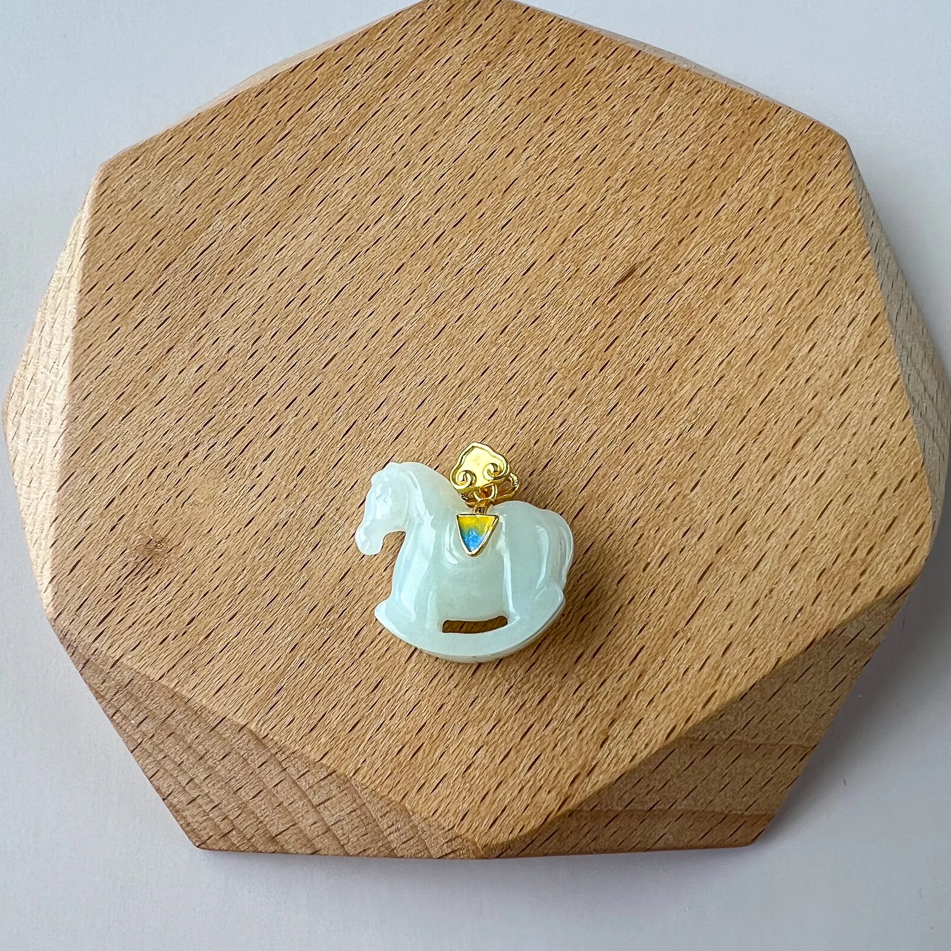Front view of jade horse pendant on wooden display base, with gold bail and iridescent accent