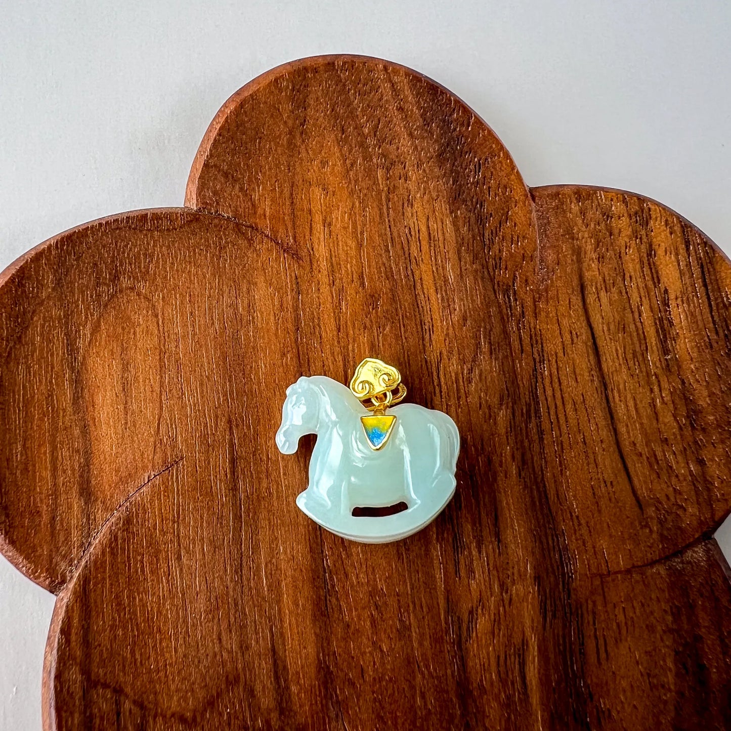 Front view of carved jade horse pendant on floral wooden stand, glossy pale green finish