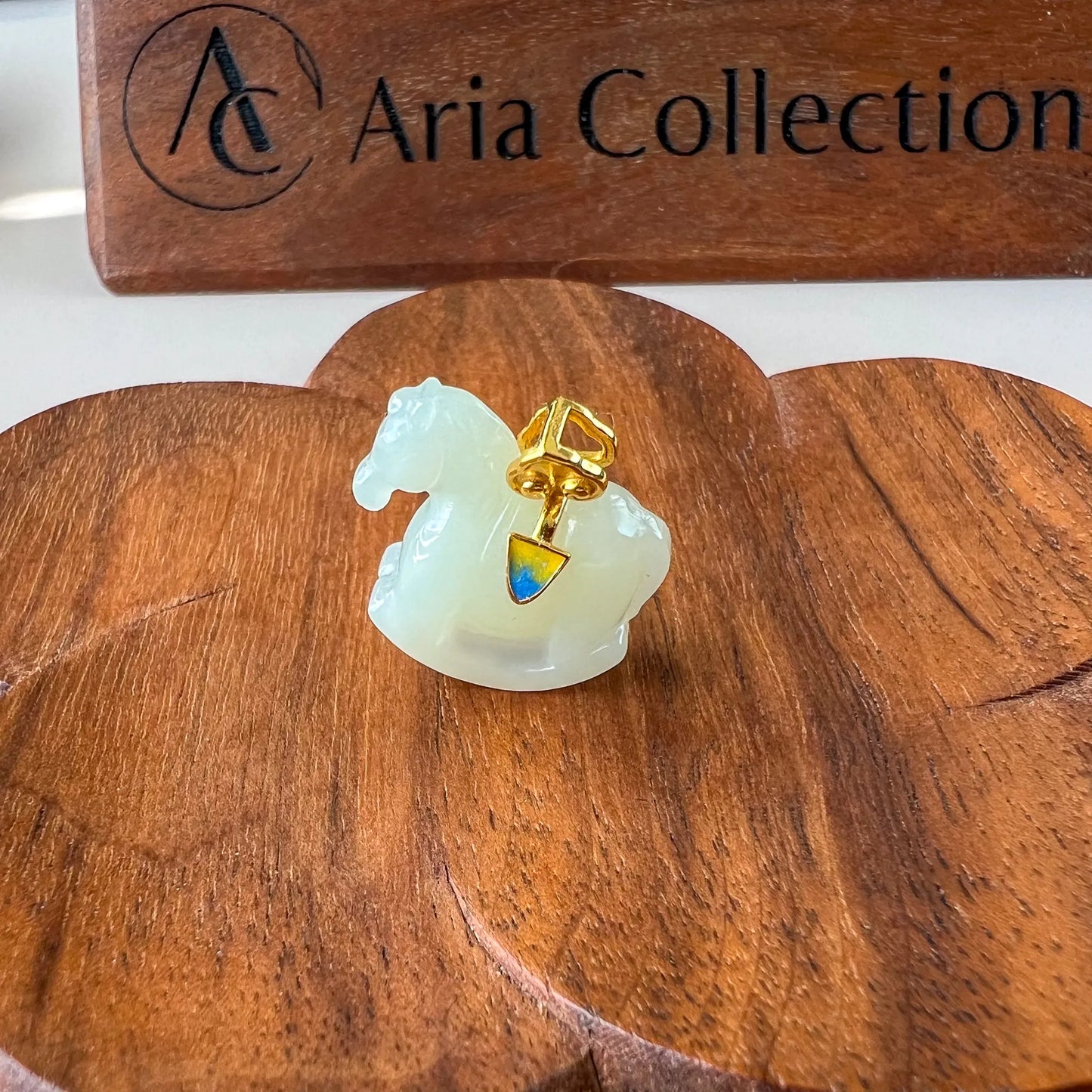 Side angle of jade horse pendant on wooden display, glossy carved stone with gold setting