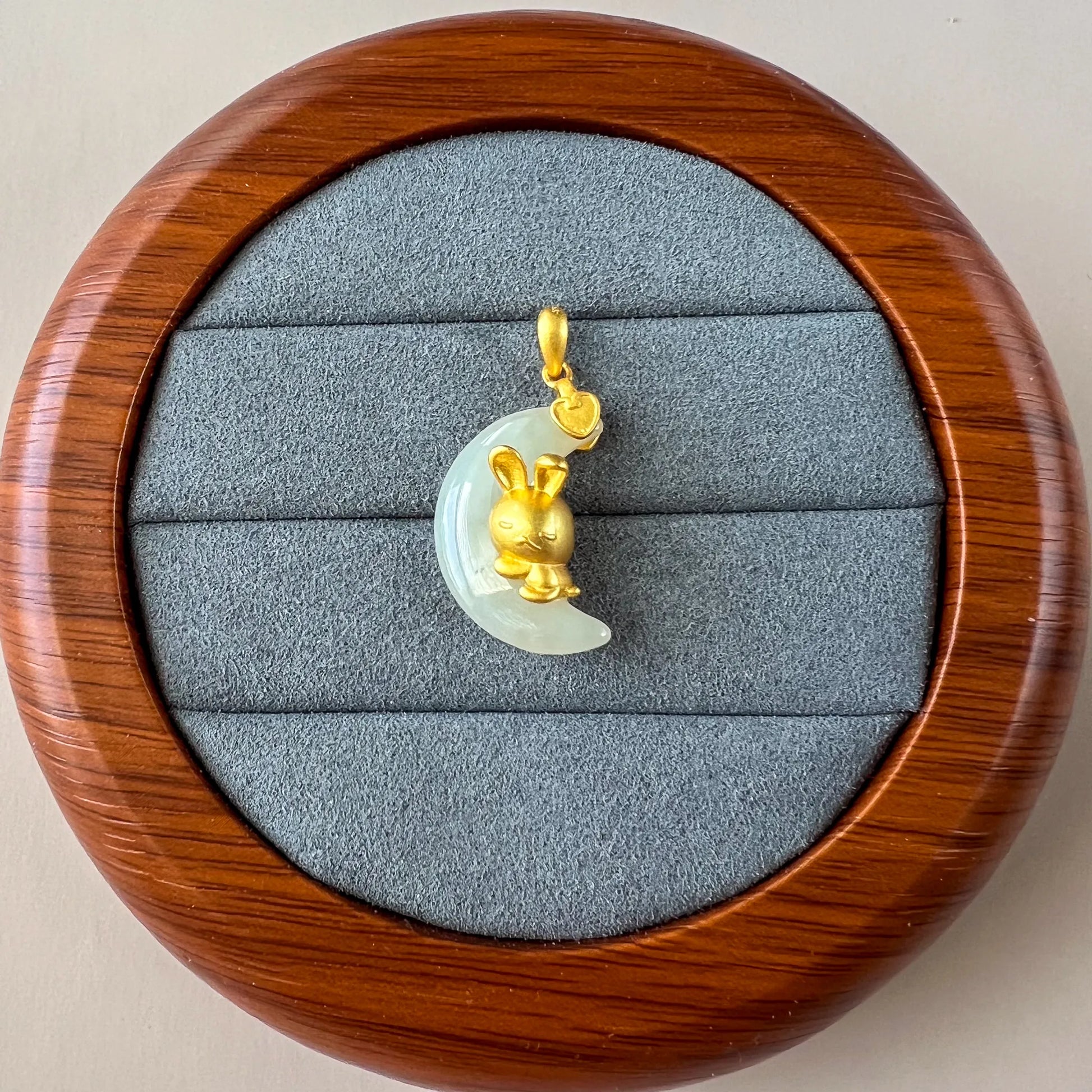 Top-down view of nephrite jade rabbit pendant with sterling silver on gray velvet display in wooden case