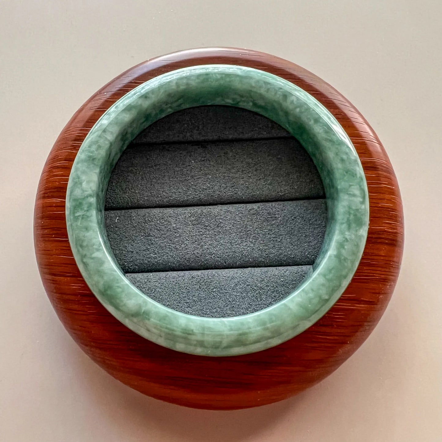 Top-down view of green jade bangle on round wood display stand, polished stone finish