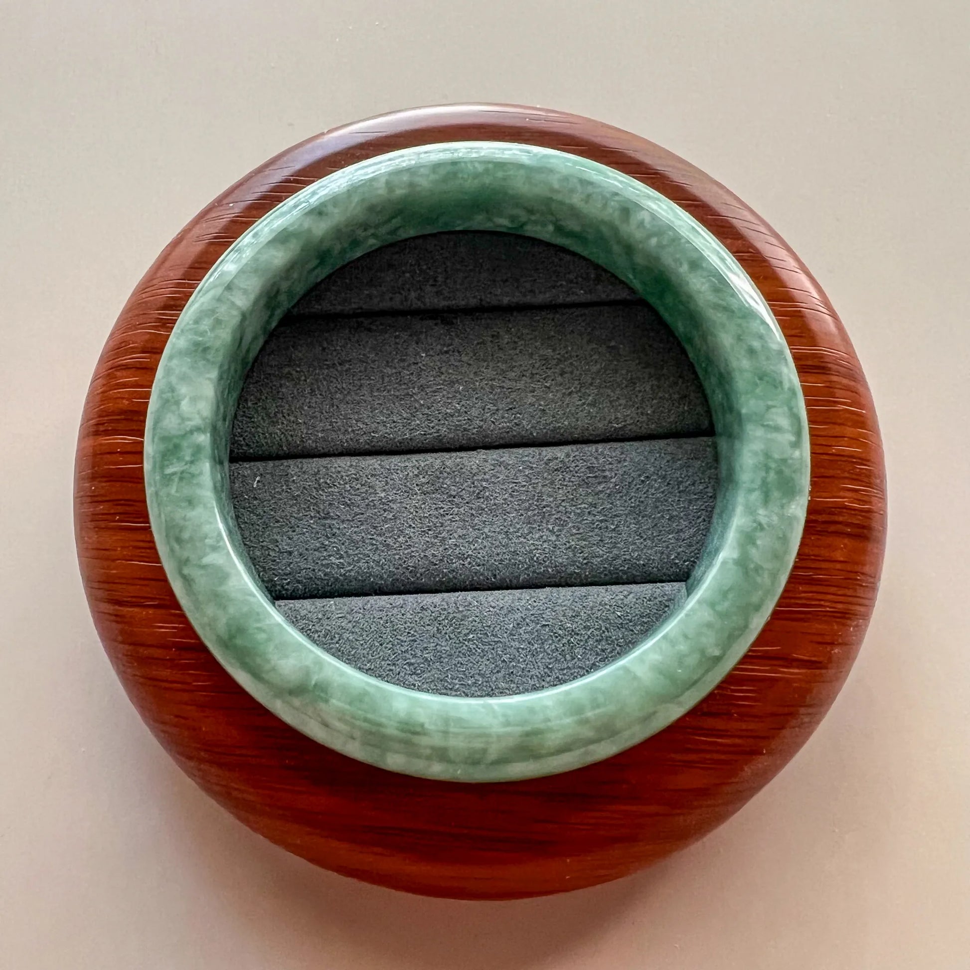 Top-down view of green jade bangle on round wood display stand, polished stone finish
