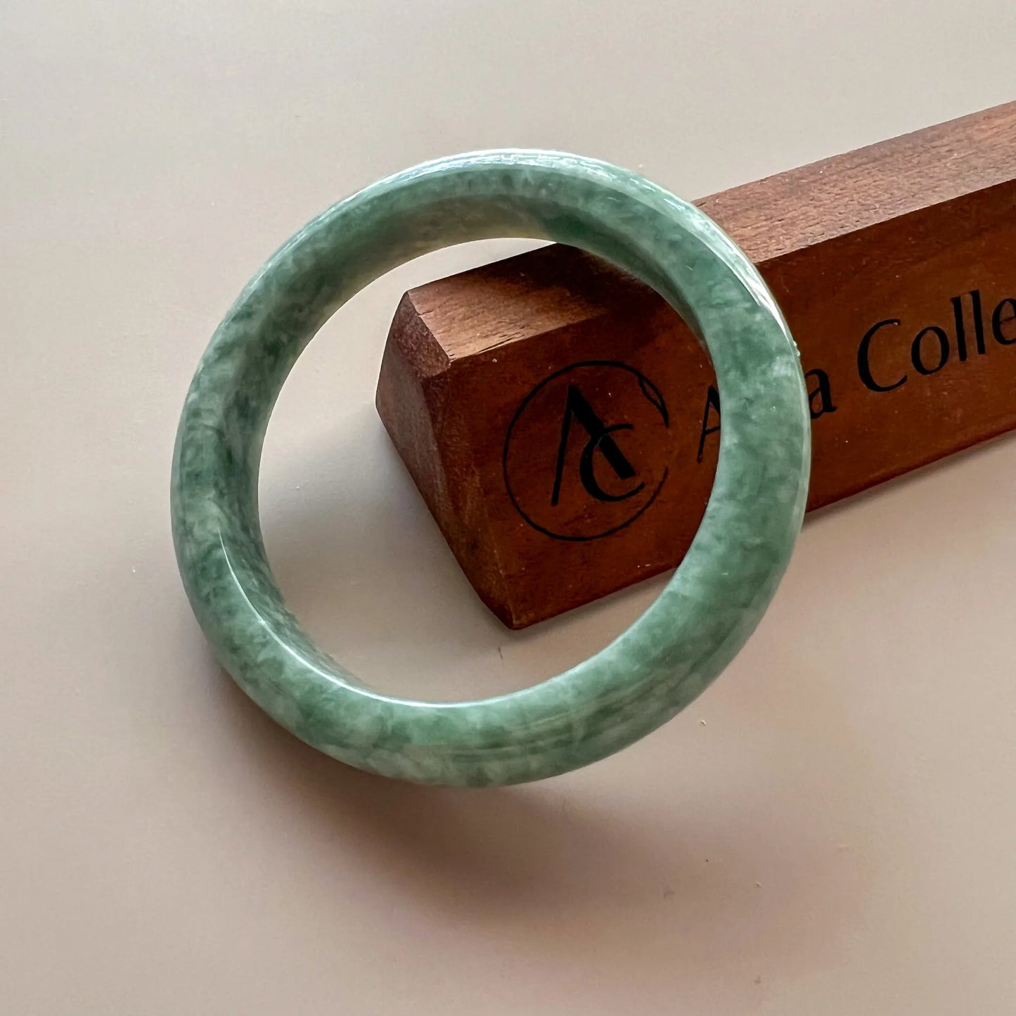 Angled front view of polished green jade bangle with wood block backdrop