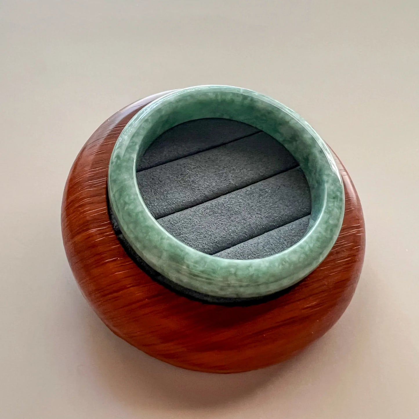 Overhead view of green jade bangle resting on carved wood stand, glossy stone surface