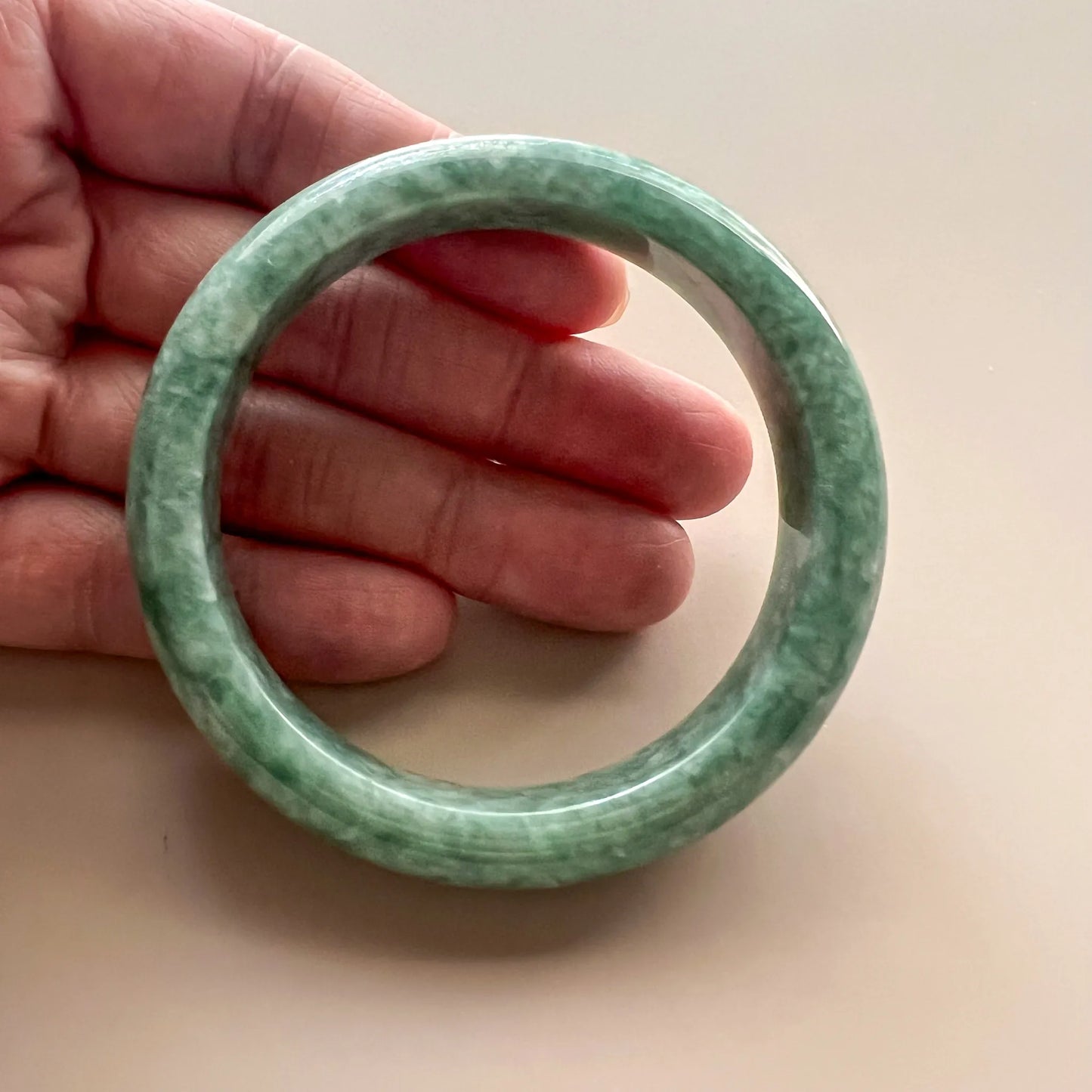 Hand-held view of the bangle showing its rounded profile, mottled green jadeite, and polished inner surface