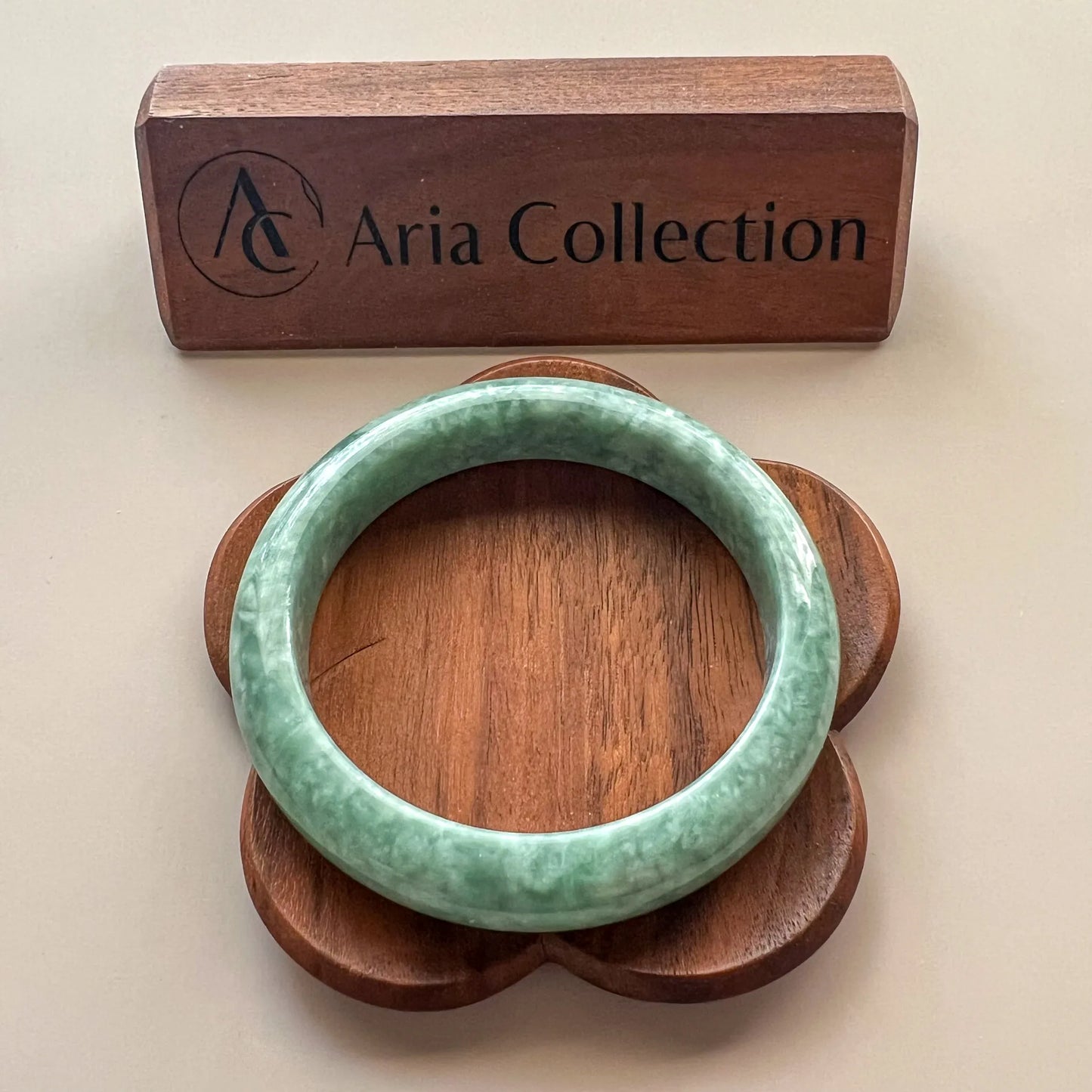 Front view of green jade bangle on floral wood stand with branded display block