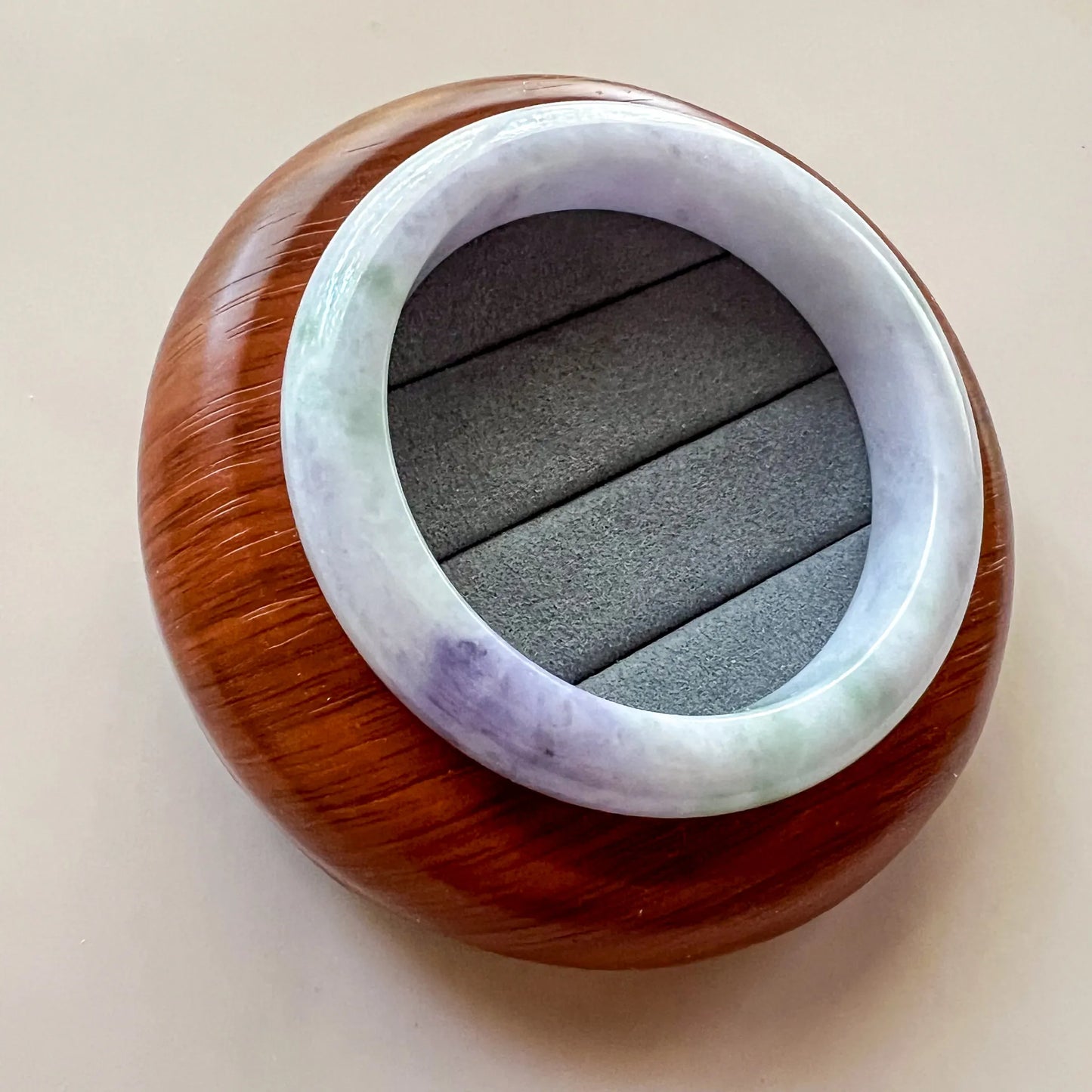 Angled view of polished jade bangle on wood display, showing lavender and green color variation