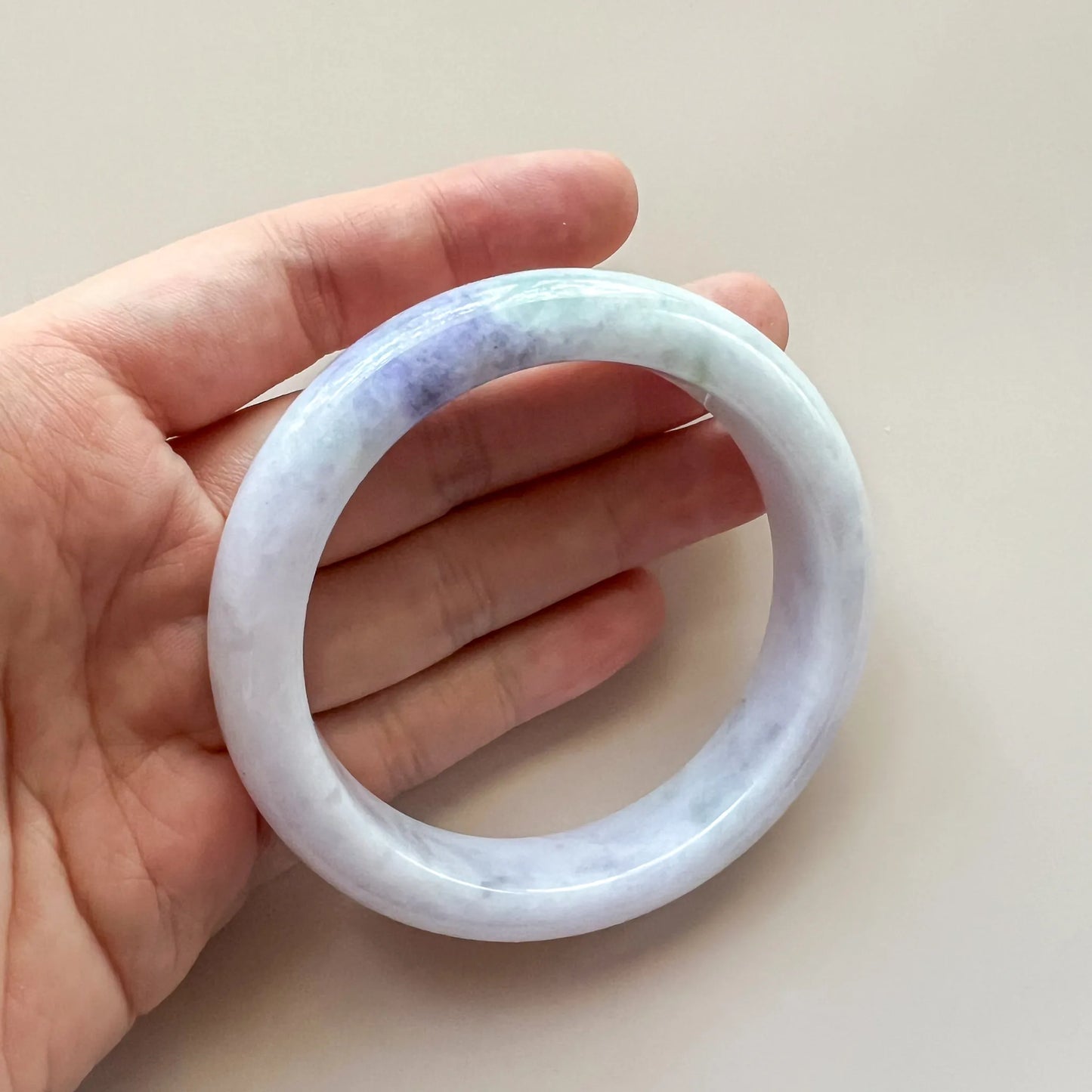Handheld view of smooth jade bangle with glossy finish and soft pastel marbling