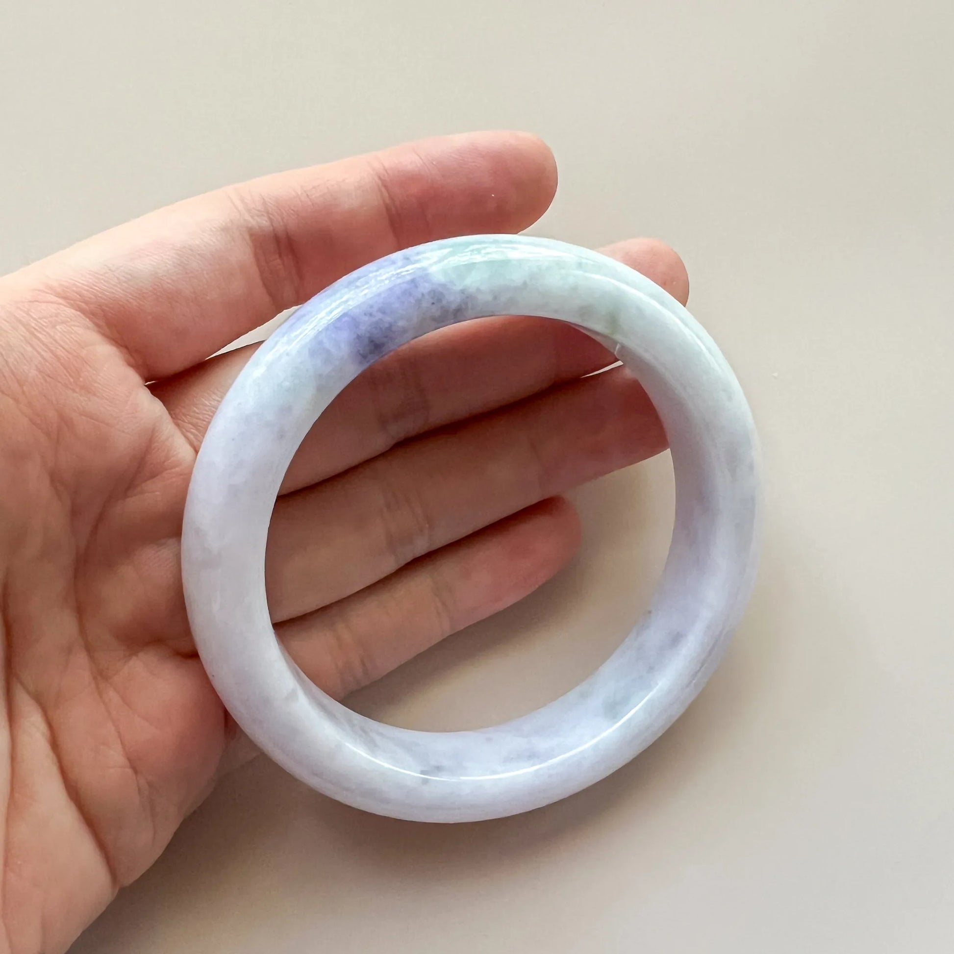 Handheld view of smooth jade bangle with glossy finish and soft pastel marbling