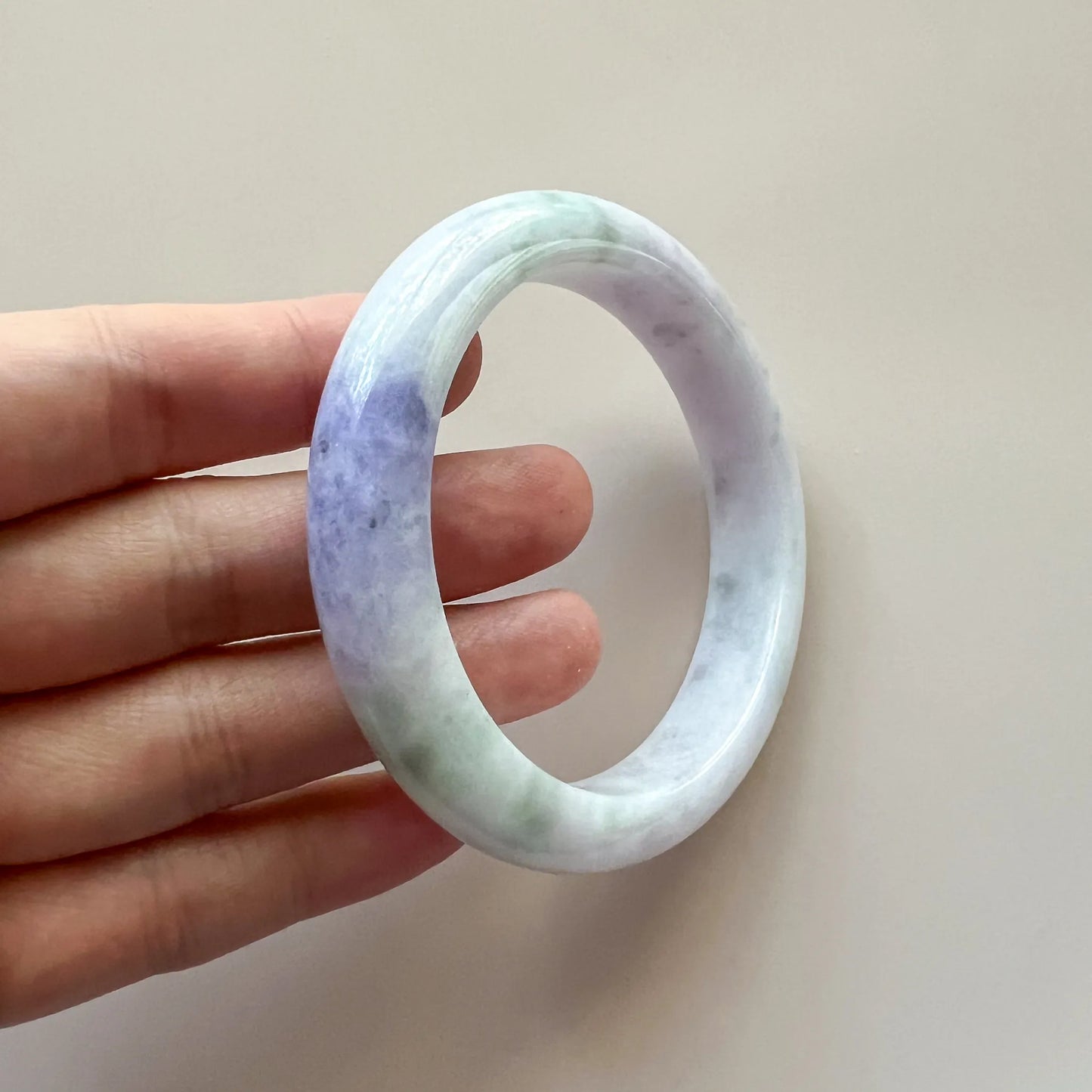Side view of oval jade bangle held in hand, polished stone surface with light green and purple tones