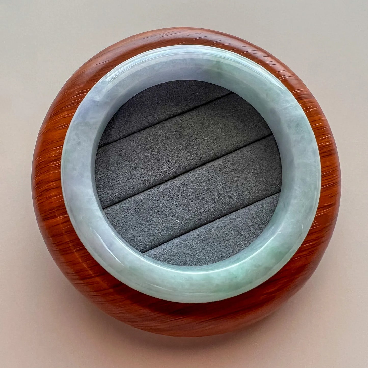 Jade bangle displayed on a wooden stand, showing glossy finish and natural color variation