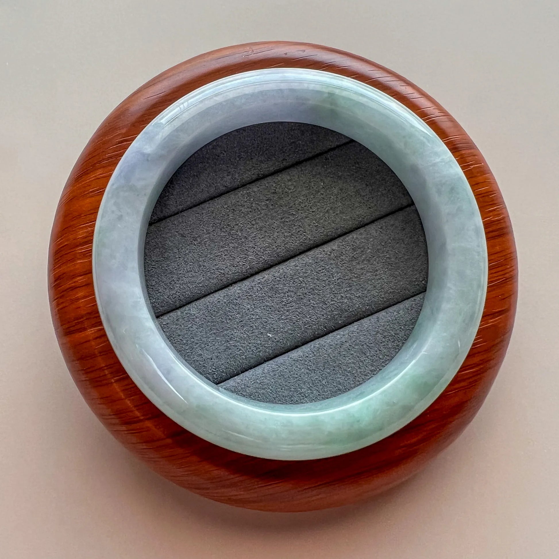 Jade bangle displayed on a wooden stand, showing glossy finish and natural color variation