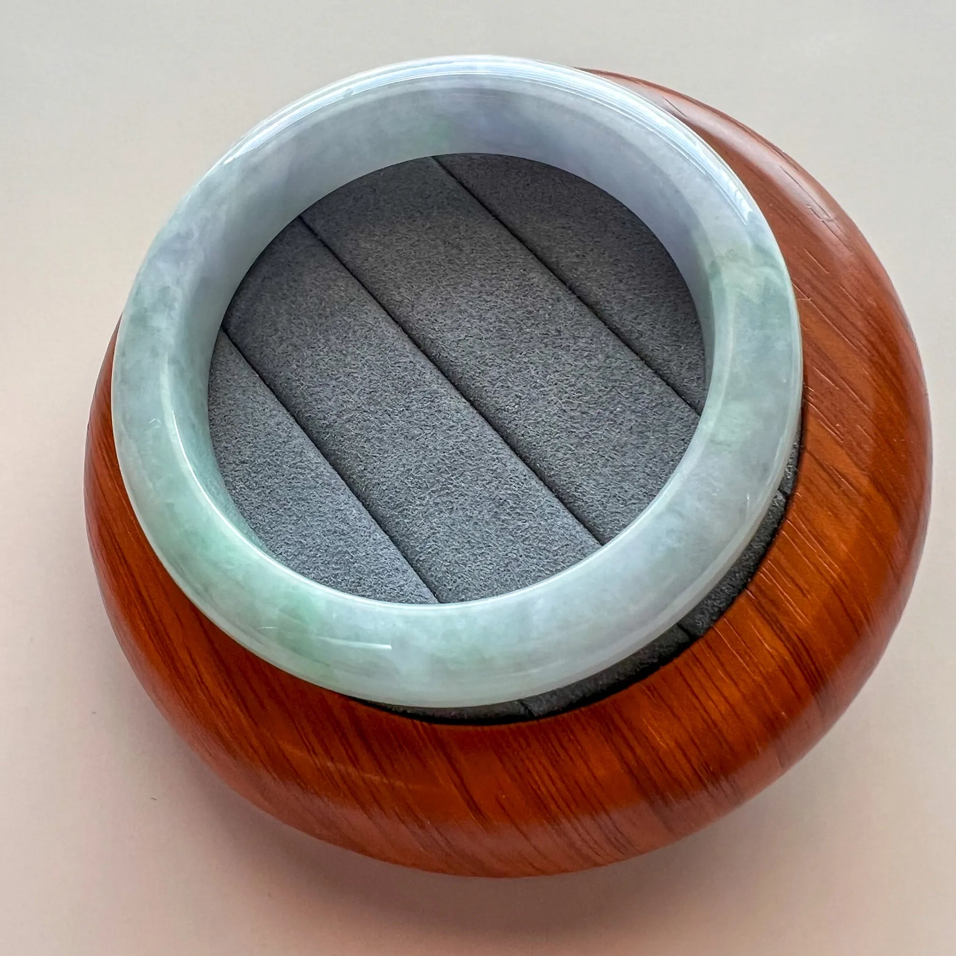 Angled view of jade bangle on carved wooden stand, highlighting smooth polished surface