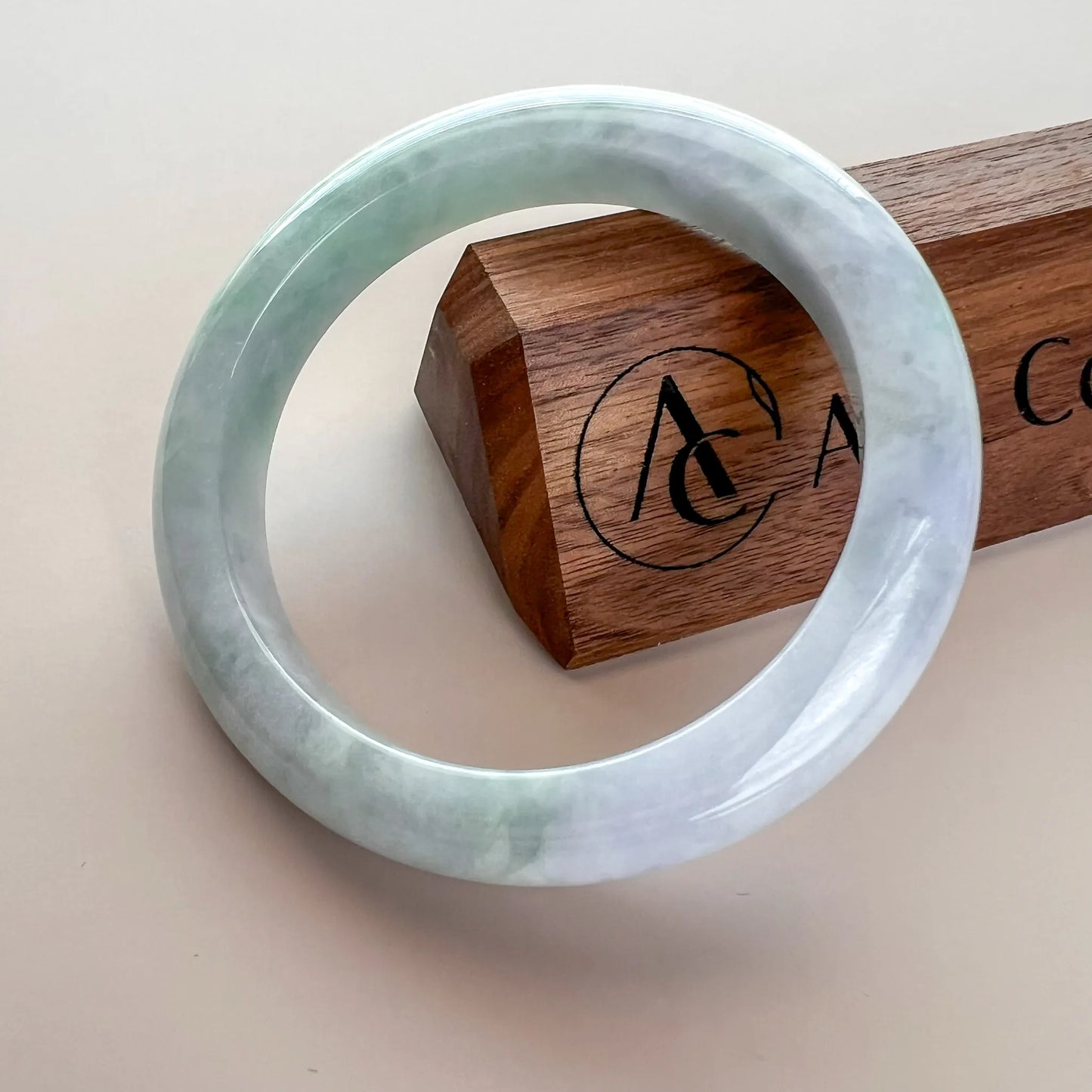 Polished jade bangle leaning against wooden display block, showing translucent green tones