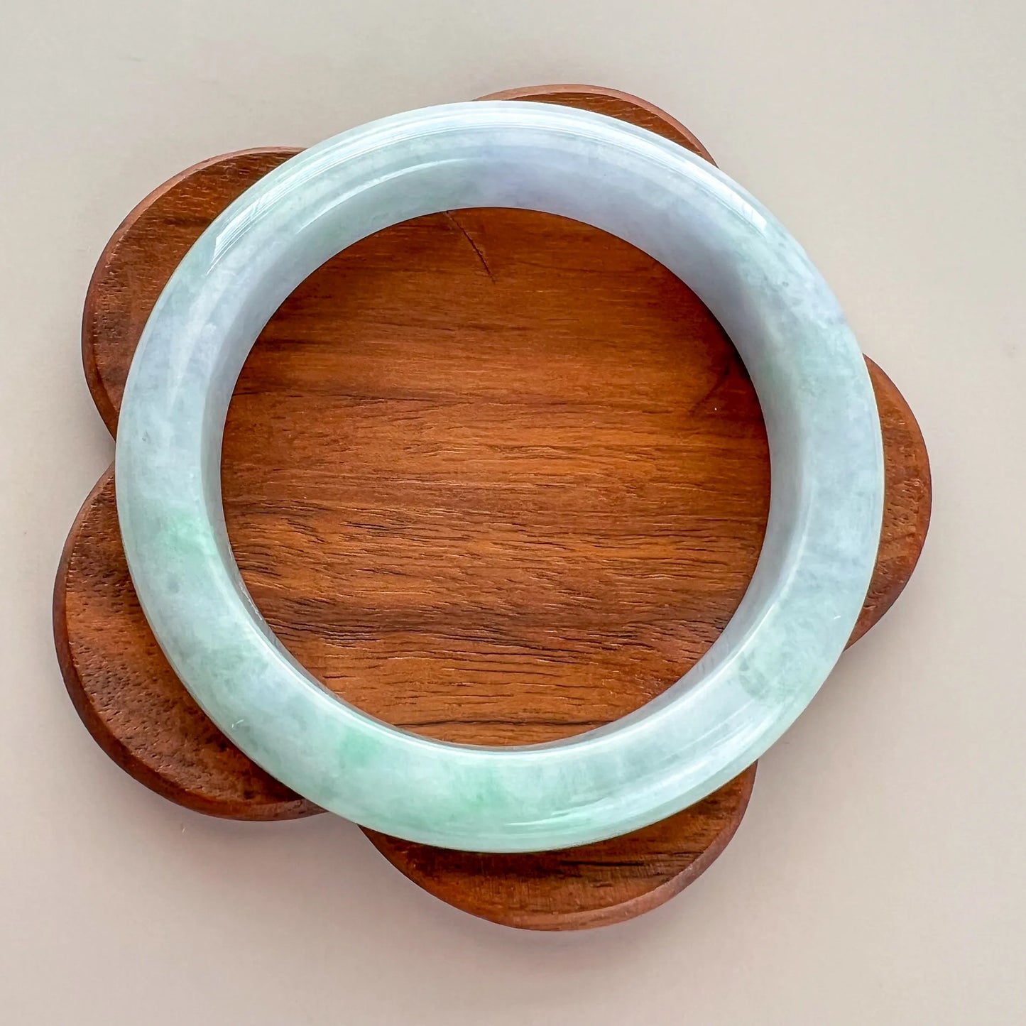 Top view of round jade bangle on wooden flower-shaped stand, glossy and smooth