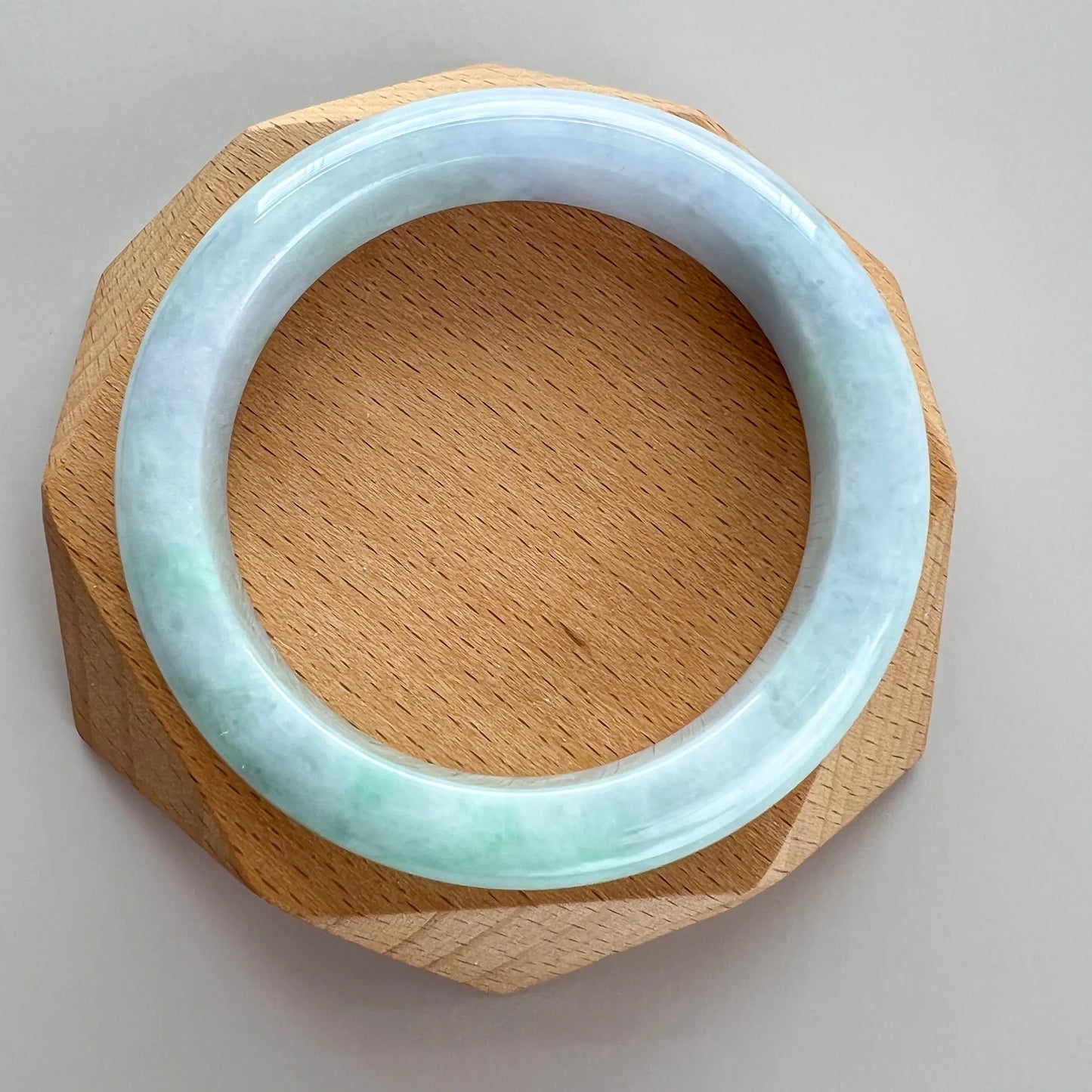 Jade bangle centered on faceted wooden stand with light green marbled finish