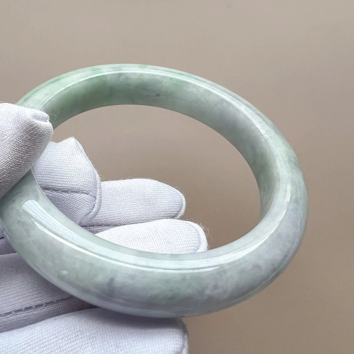 Angled side profile of an icy light green-gray jadeite bangle showing its rounded shape and polished surface