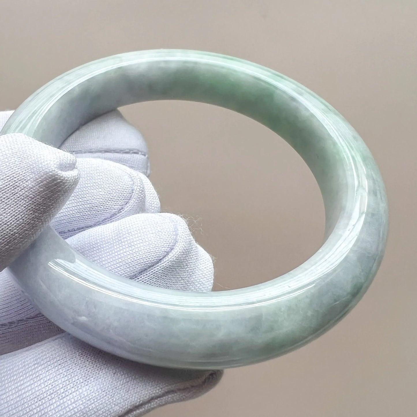 Close-up side view of jade bangle held by gloved hand, showing rounded profile and sheen