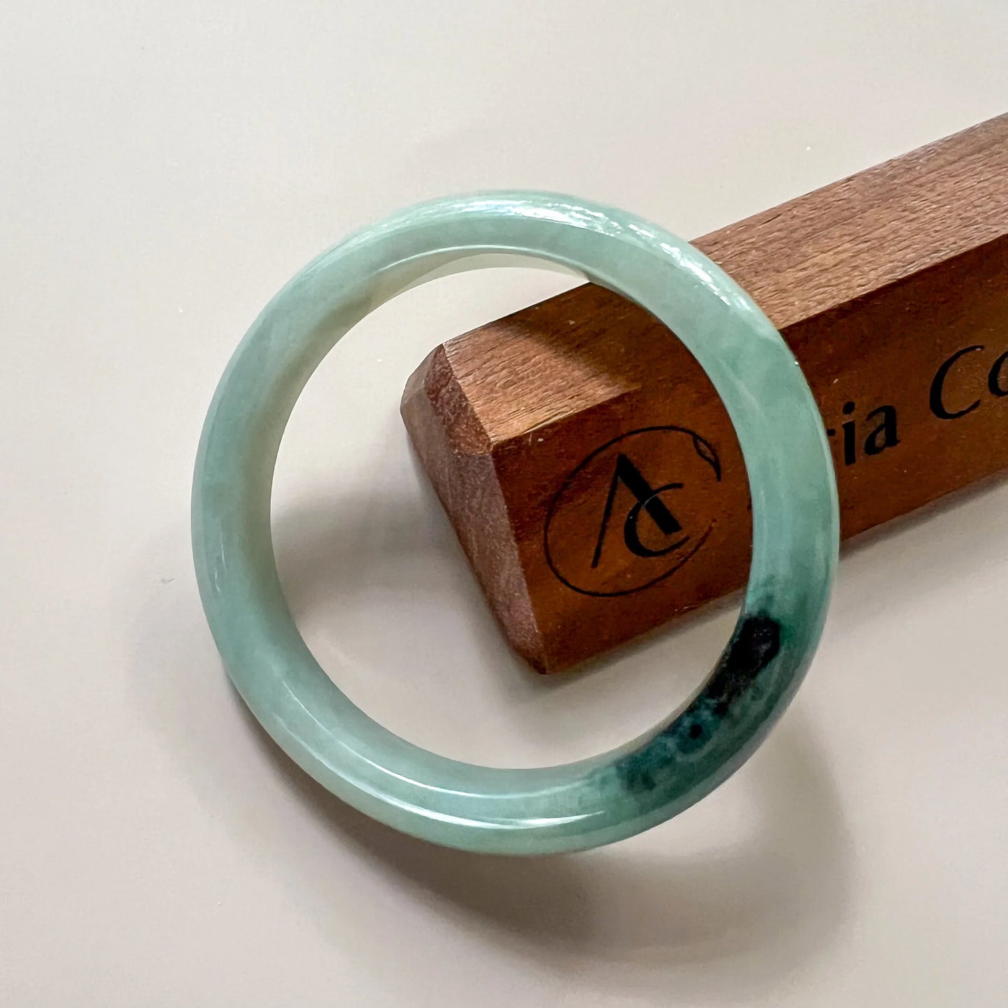 Front view of polished pale green jade bangle with dark inclusions on display stand