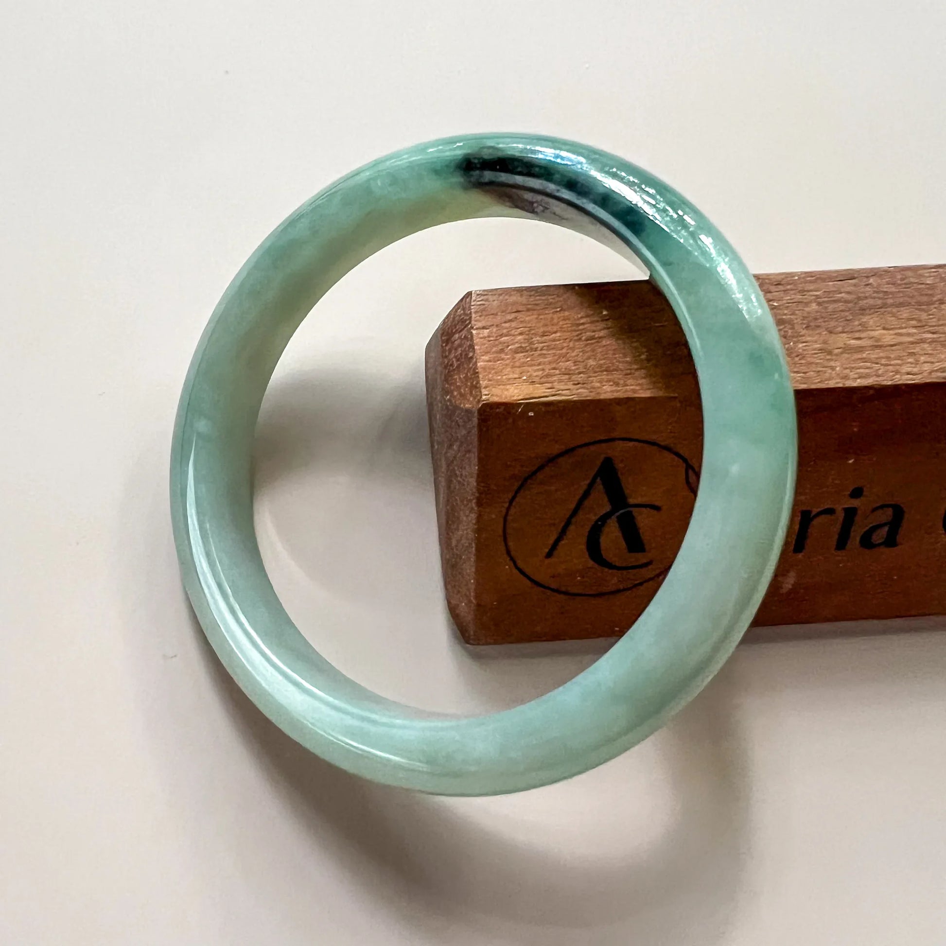 Straight-on view of smooth jade bangle with glossy finish and dark mottled accent
