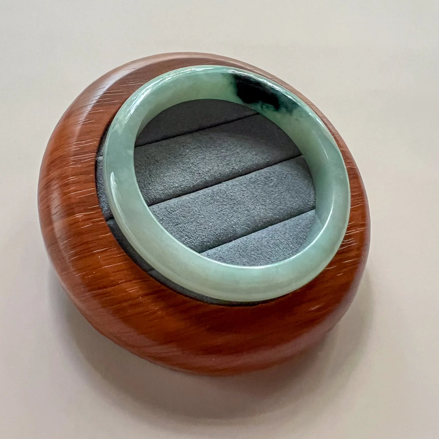Angled view of polished jade bangle resting on suede-lined round wood stand