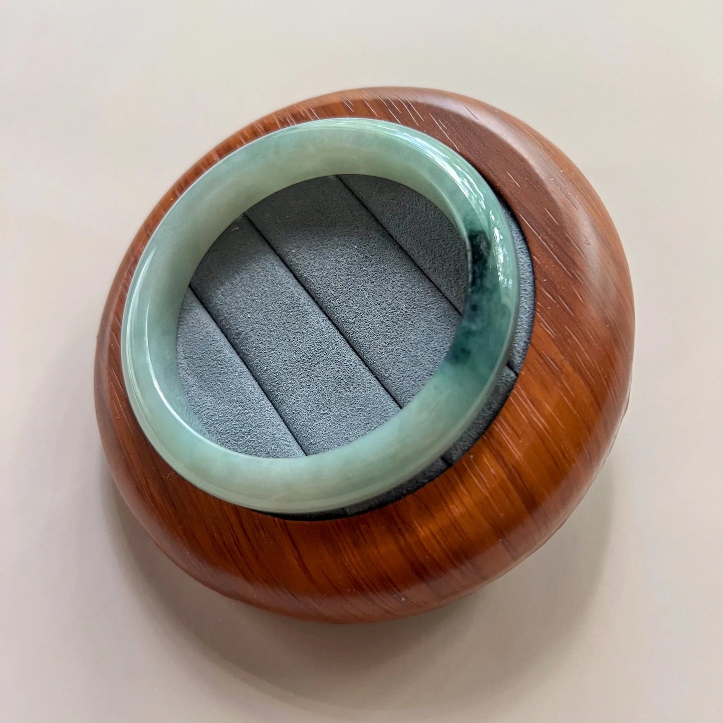 Top angled view of glossy jade bangle in wood presentation holder with suede insert