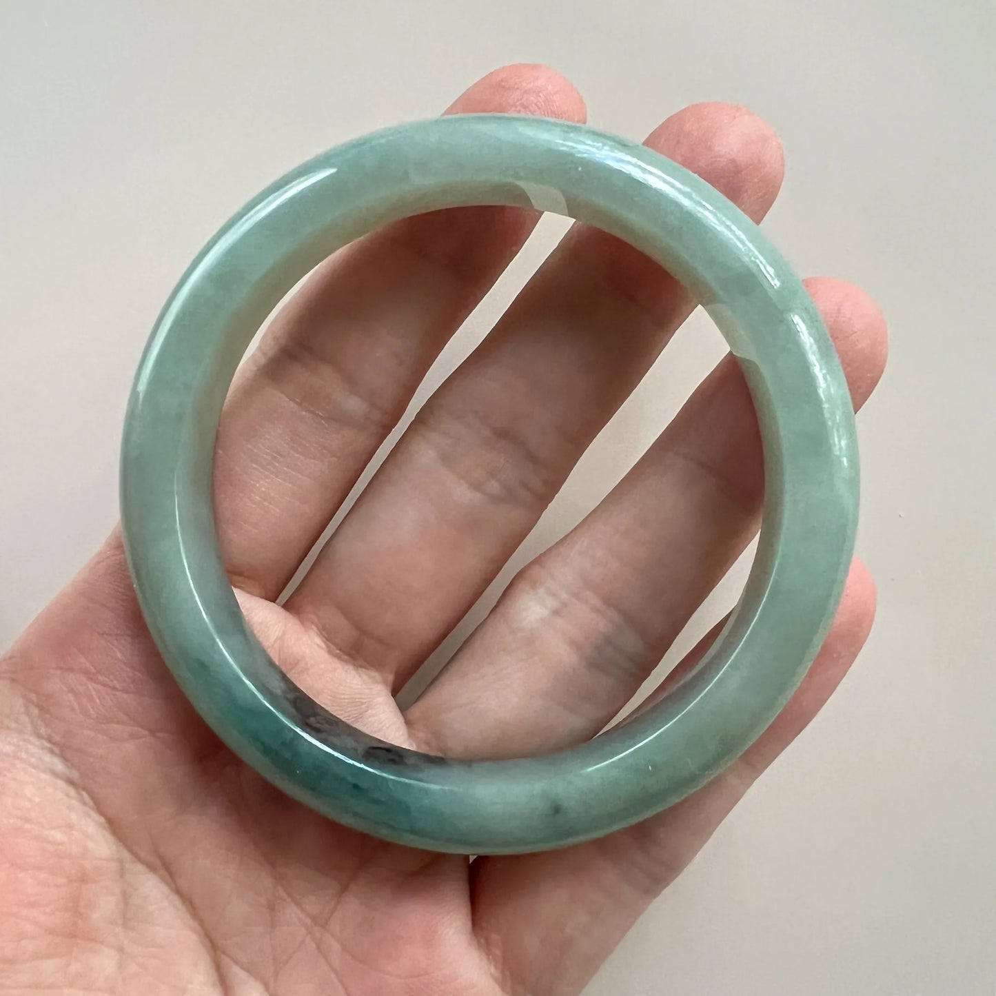 Handheld front view of translucent green jade bangle with polished surface